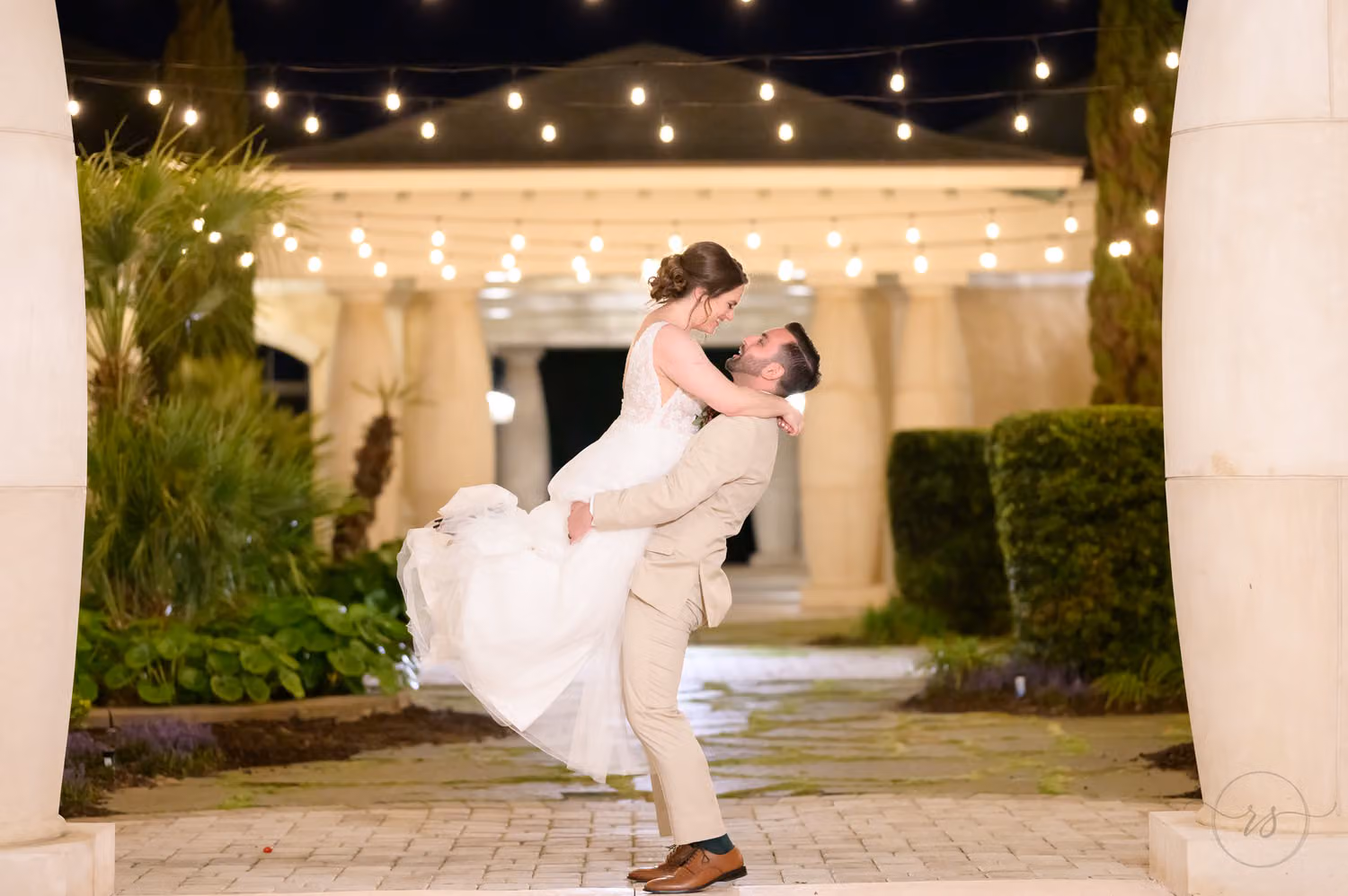 Groom lifting the bride into the air under string lights in the courtyard at night at 21 Main Events