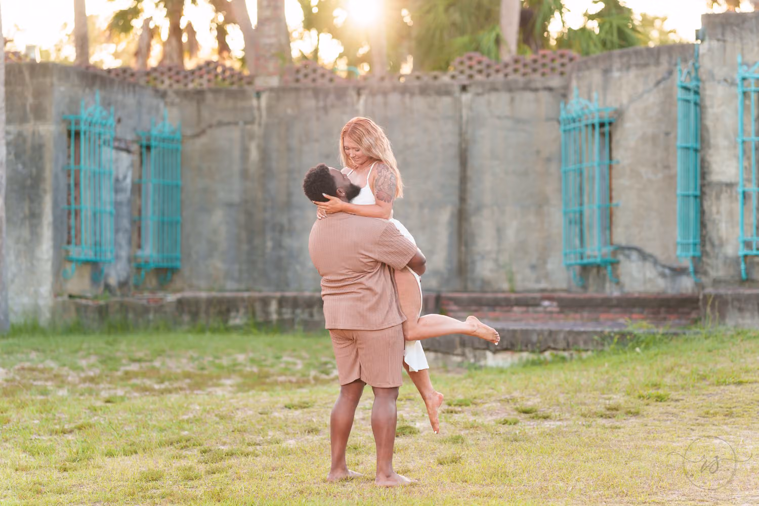 Man lifting his fiancée as she kicks up a foot in front of the old castle wall at Huntington Beach State Park