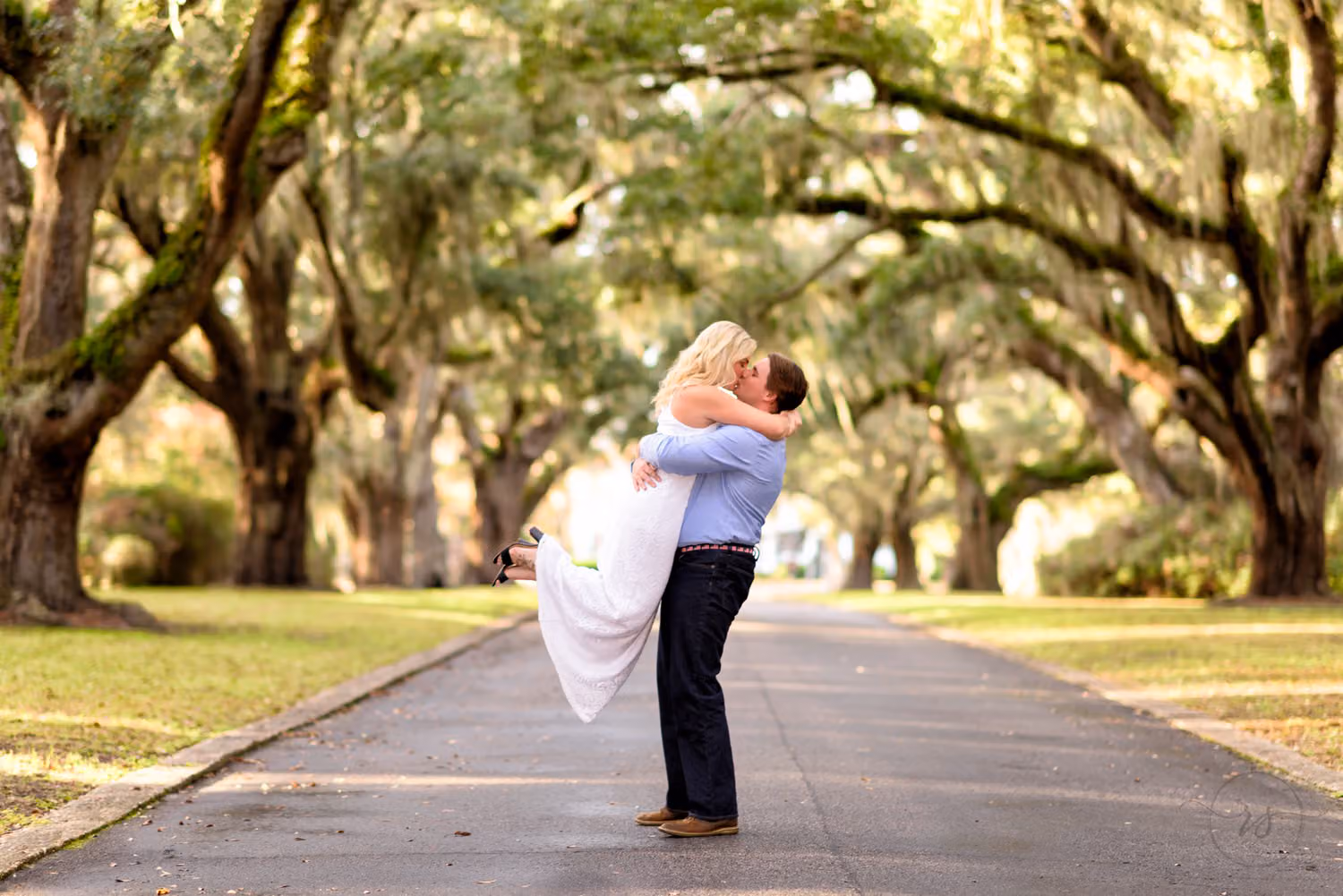 Man lifting his fiancée into the air on a long avenue of live oaks at Litchfield Plantation