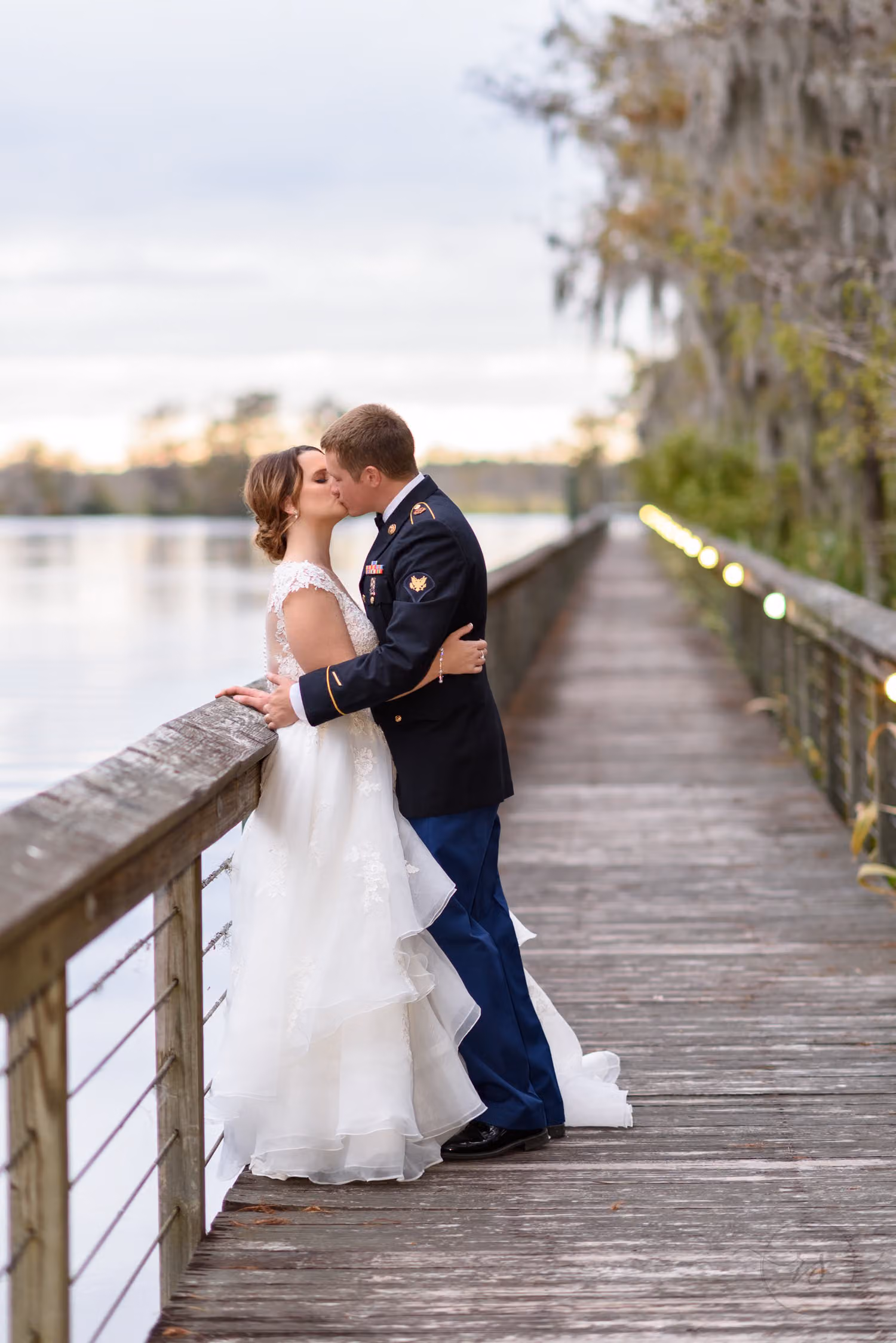 Bride and groom kissing at the railing of a long boardwalk over the water at dusk at Reserve Harbor Yacht Club