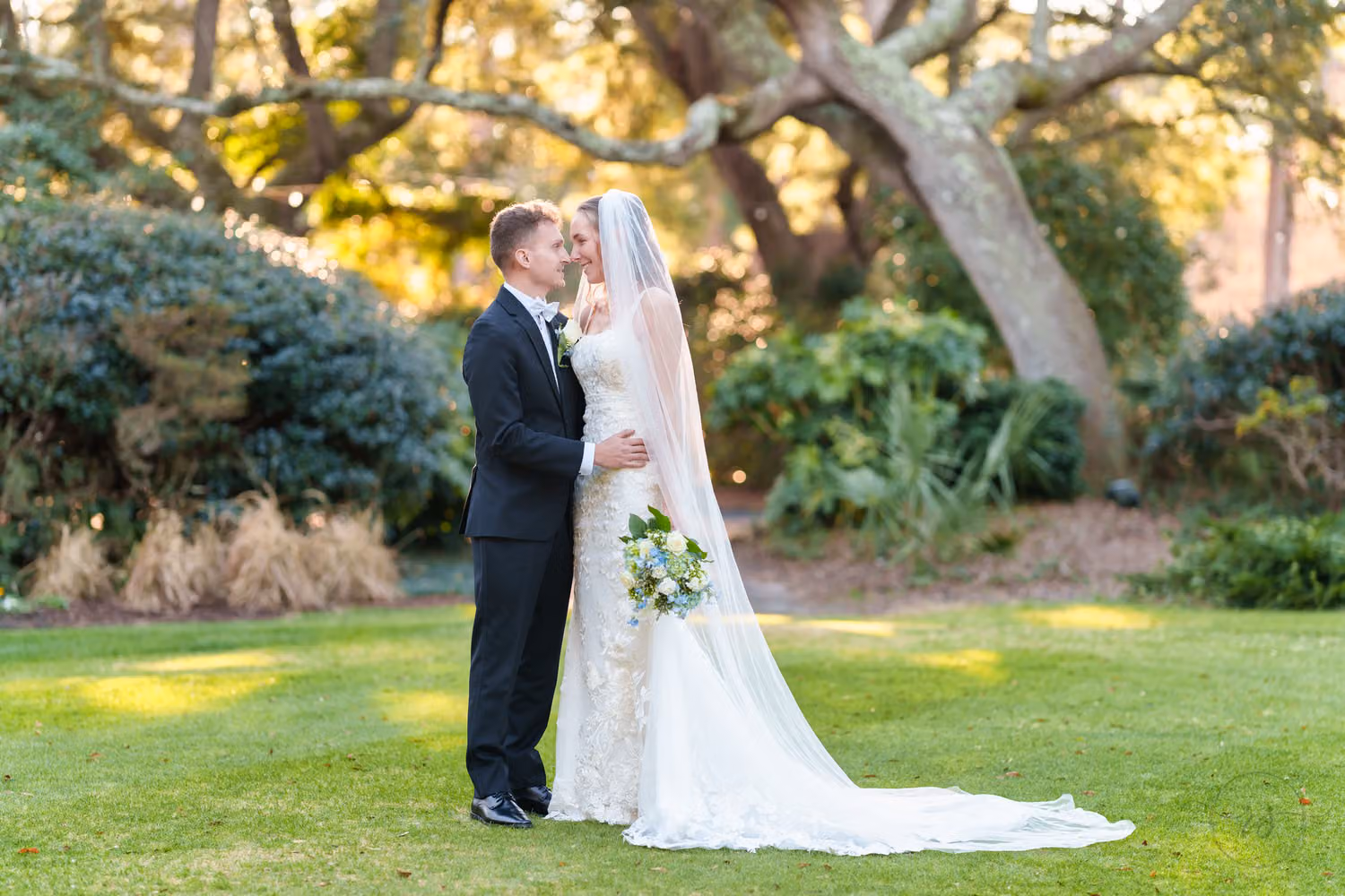 Bride in a long veil and groom gazing at each other on the lawn in front of the oaks at Litchfield Country Club
