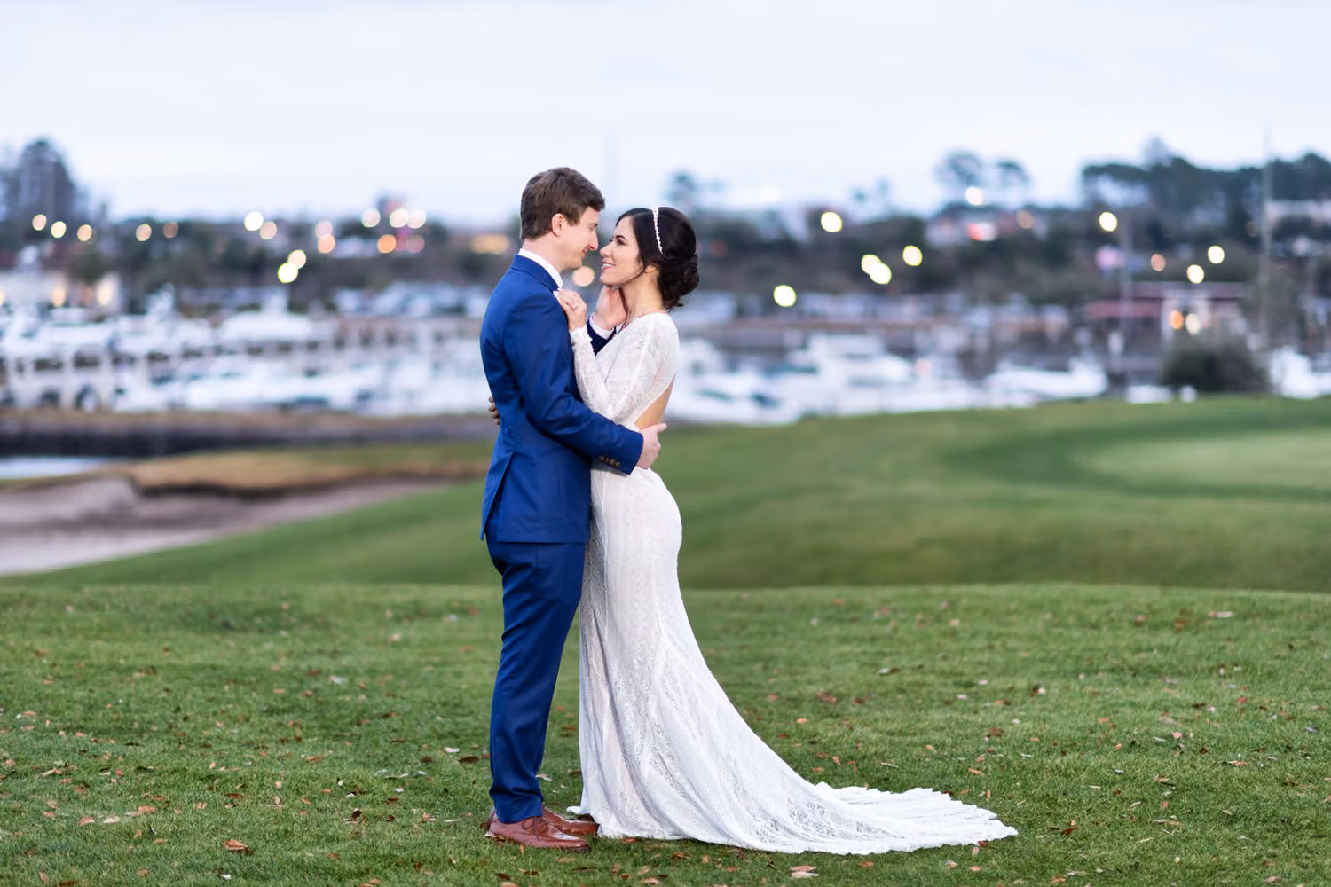 Bride and groom touching foreheads on the golf course with marina boats behind them at Grande Dunes in Myrtle Beach