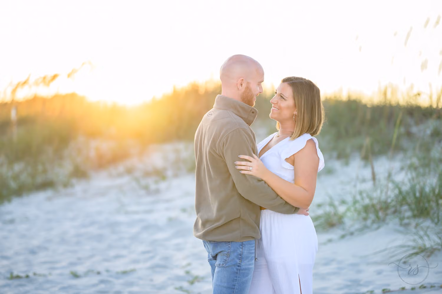 Couple gazing at each other as the sunset glows over the dunes and sea oats behind them at Huntington Beach State Park