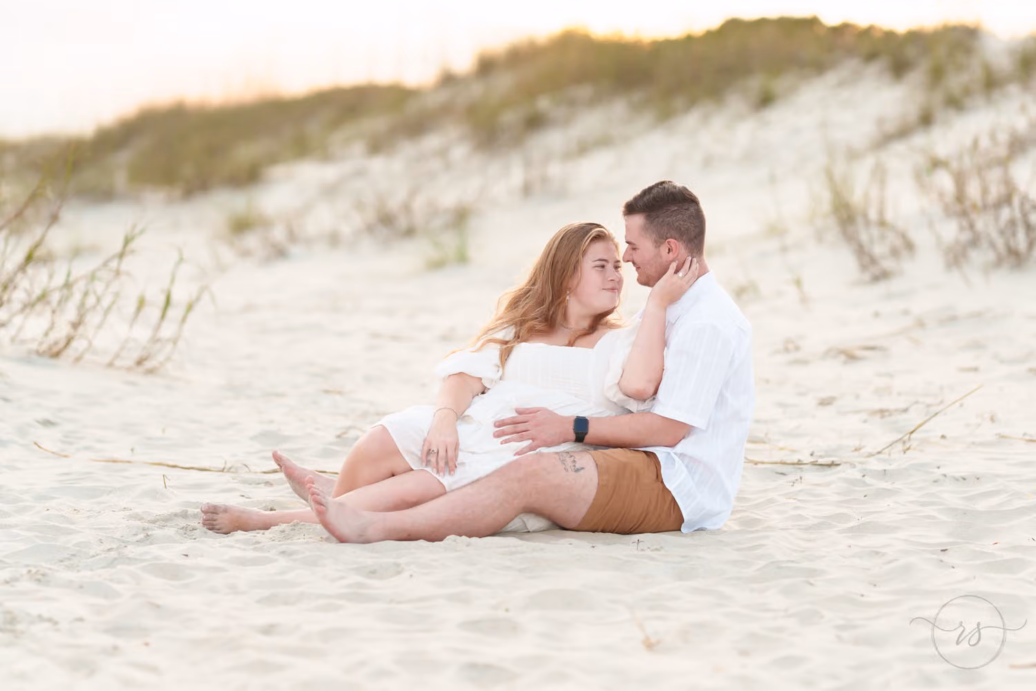 Couple lounging in the sand by the dunes, gazing at each other at Huntington Beach State Park