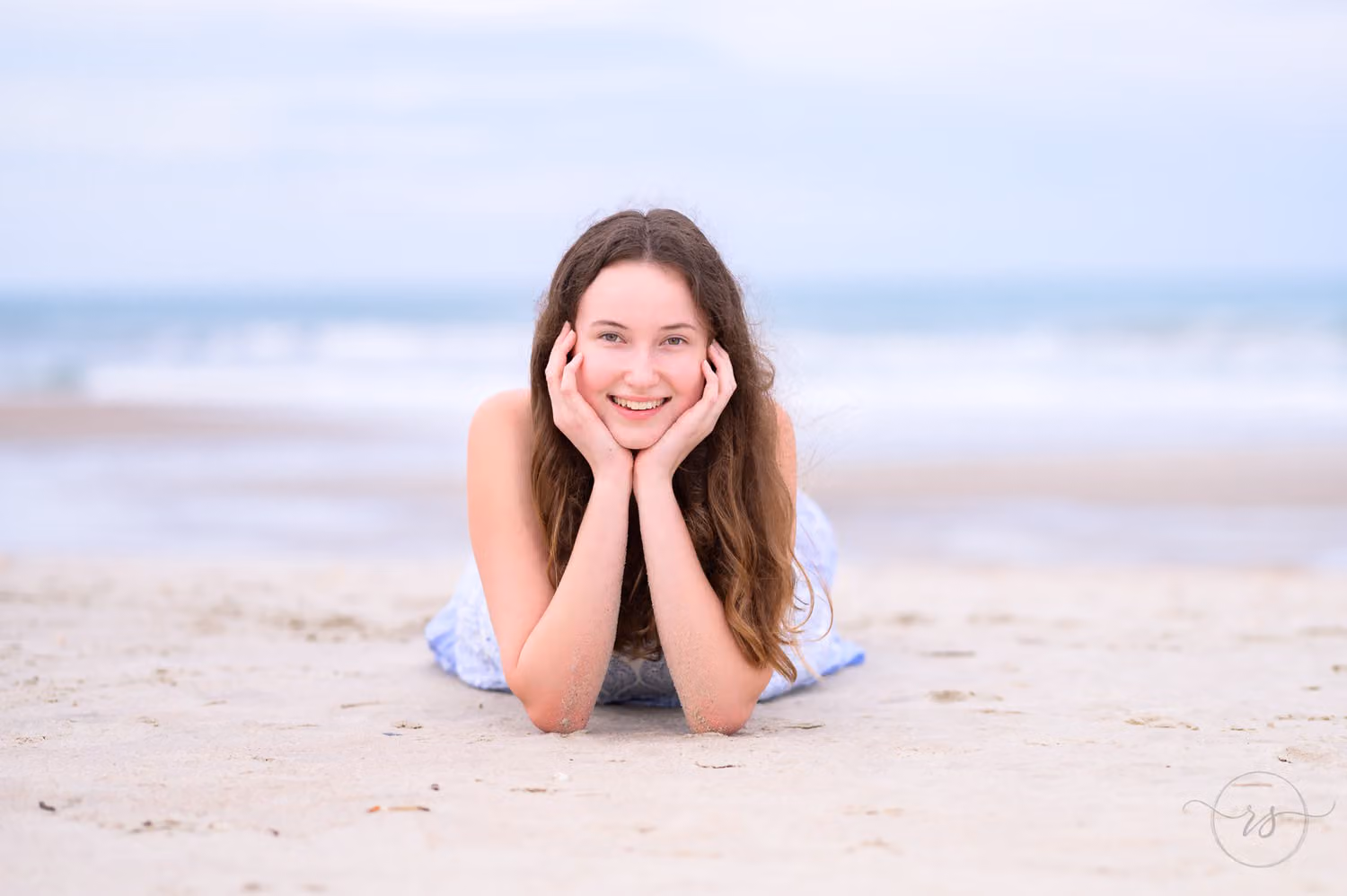 Smiling senior lying on the beach with her chin resting in both hands at Huntington Beach State Park