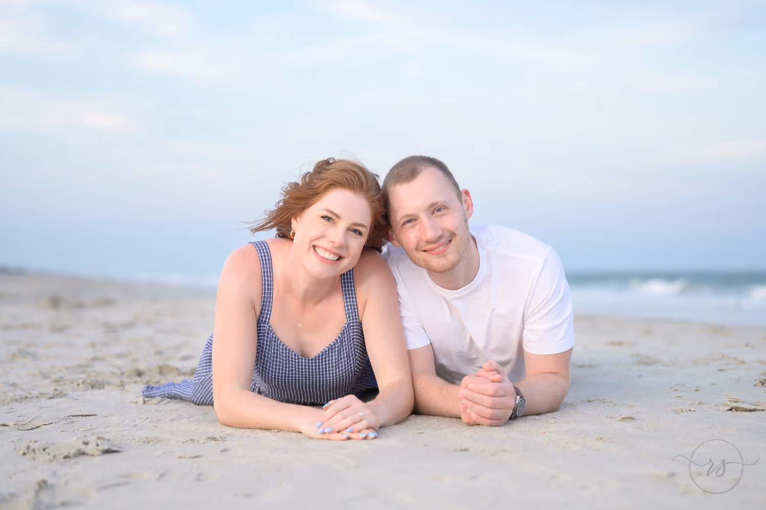 Couple lying on their stomachs side by side on the sand under a blue sky at Huntington Beach State Park