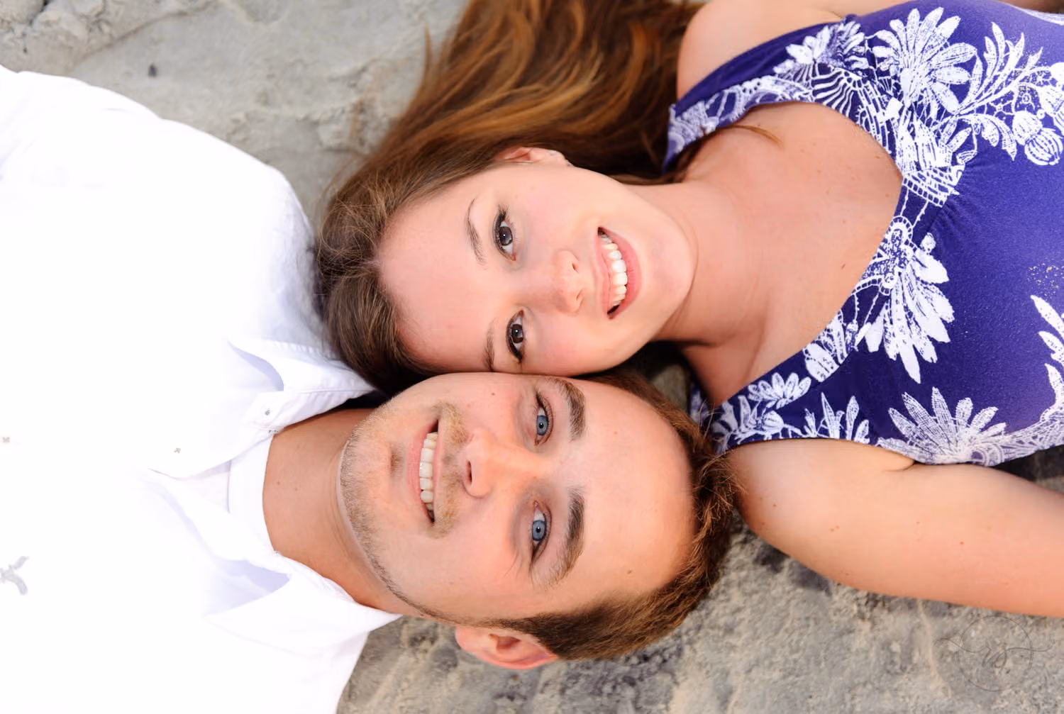 Couple lying face up in the sand with their heads together, smiling at the camera at Myrtle Beach State Park