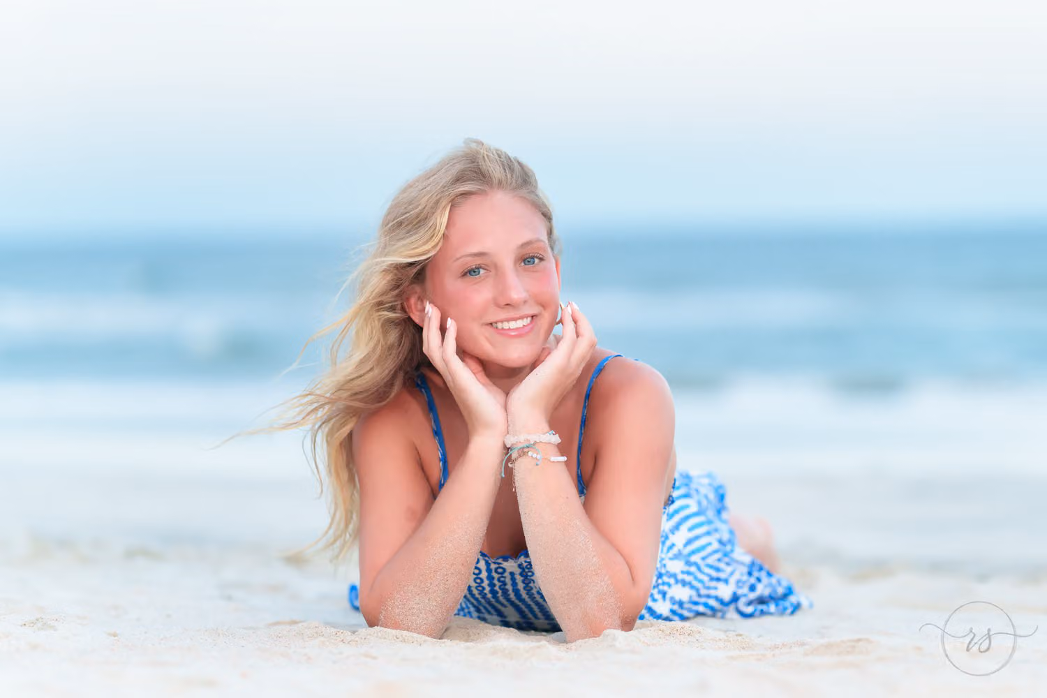 Senior girl lying on her stomach in the sand with her chin in her hands by the ocean at Huntington Beach State Park