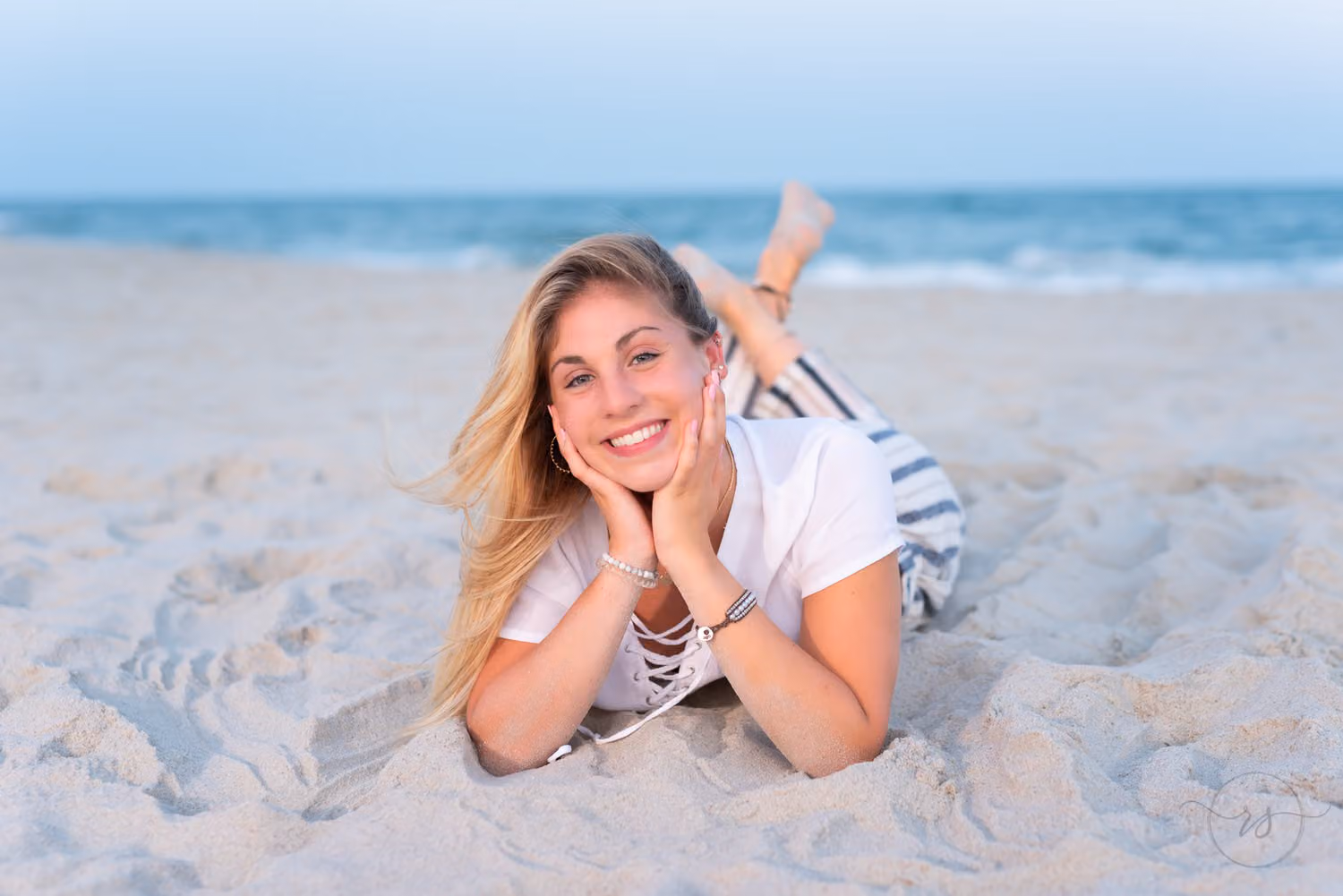 Smiling senior lying on her stomach in the sand with her chin in her hands at Huntington Beach State Park