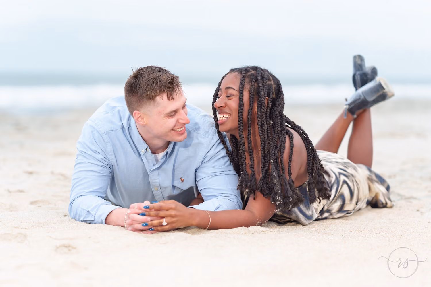 Couple lying on their stomachs in the sand, laughing with their feet kicked up at Huntington Beach State Park