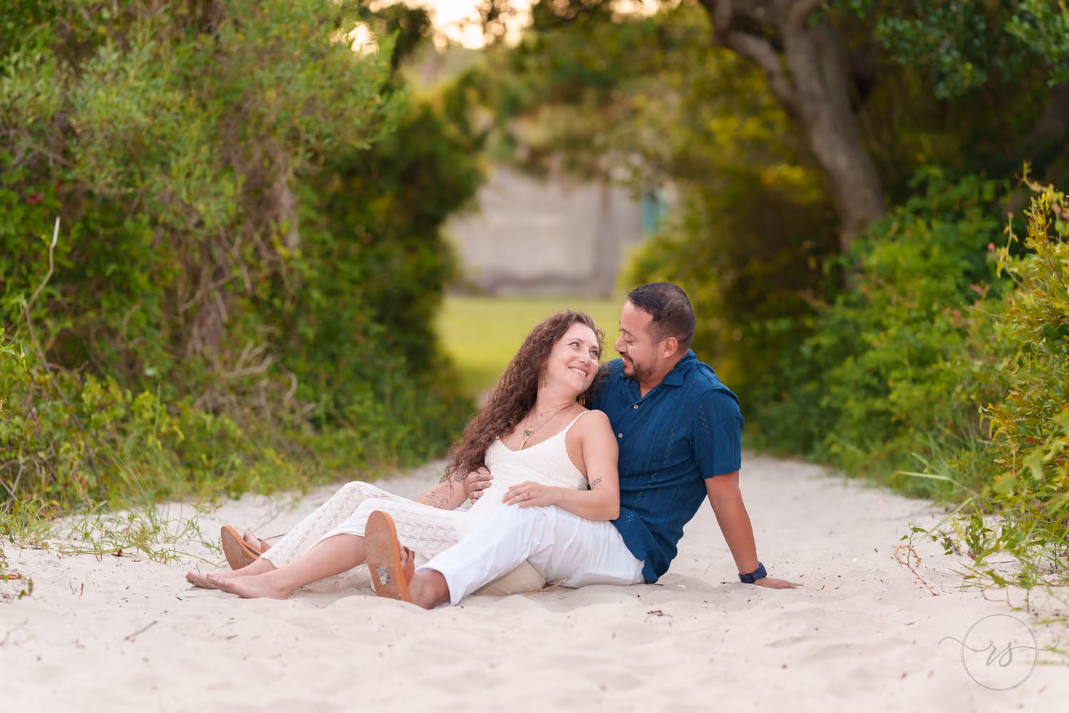 Couple in white and navy lounging in the sand on a beach path framed by green brush at Huntington Beach State Park