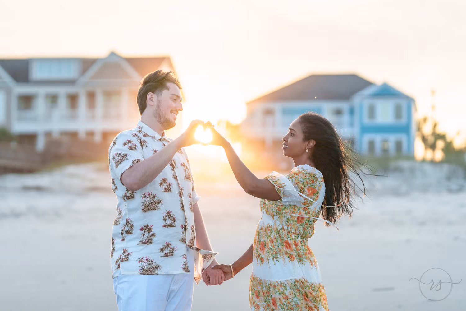 Couple in floral outfits shaping a heart with their hands around the setting sun between beach houses in Pawleys Island