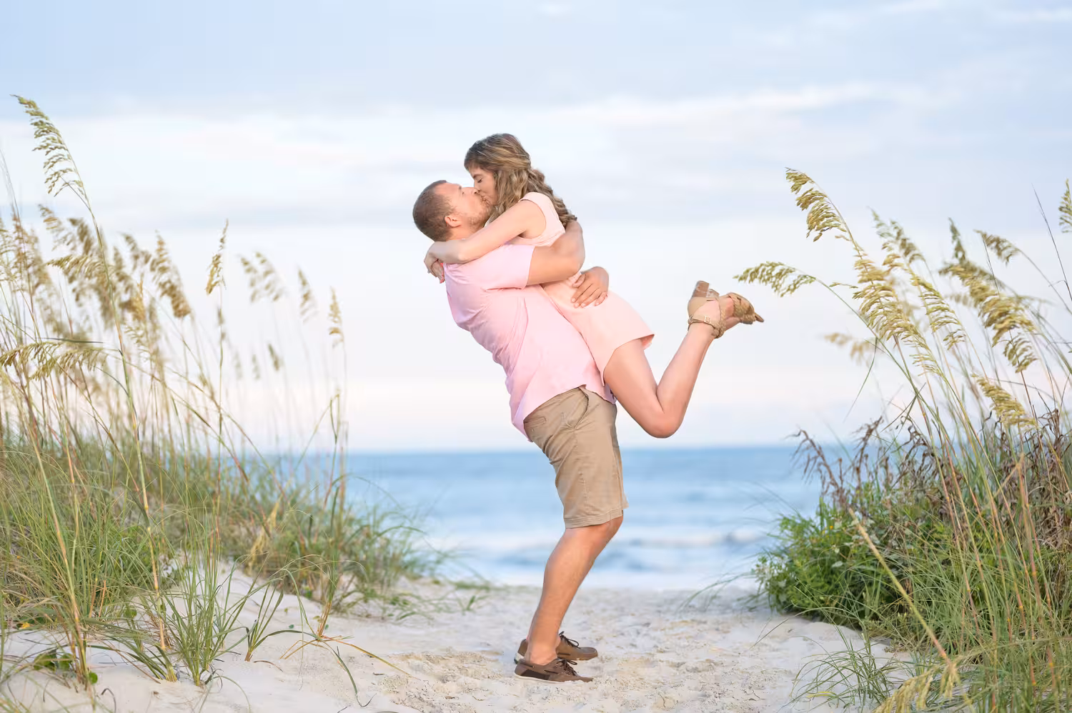 Man lifting his partner for a kiss by the sea oats at Huntington Beach State Park