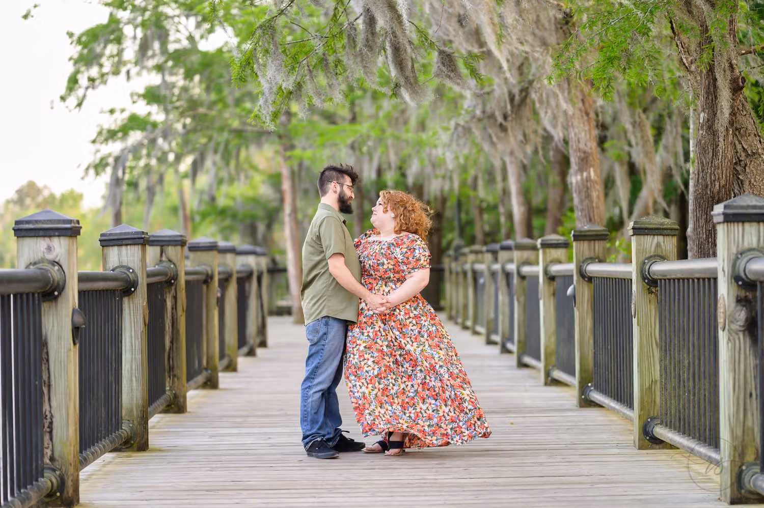 Couple holding each other on a wooden boardwalk under oaks hung with Spanish moss along the Conway Riverwalk