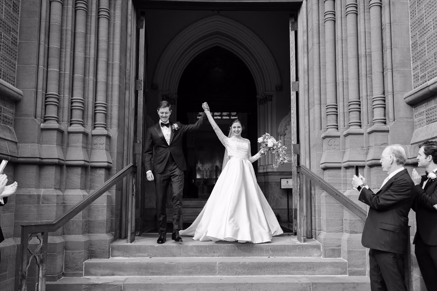 Bride raising her arm as the newlyweds leave the cathedral doors, in black and white, at the Cathedral of Saint John