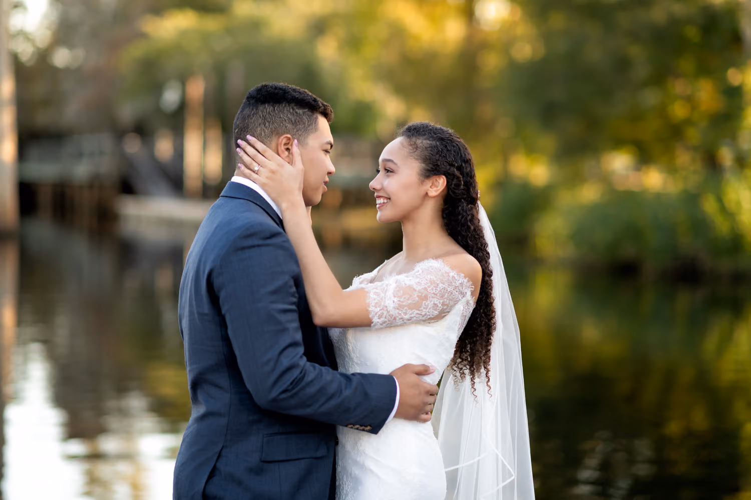 Couple in wedding attire holding each other and smiling by the river in warm evening light at the Conway Riverwalk