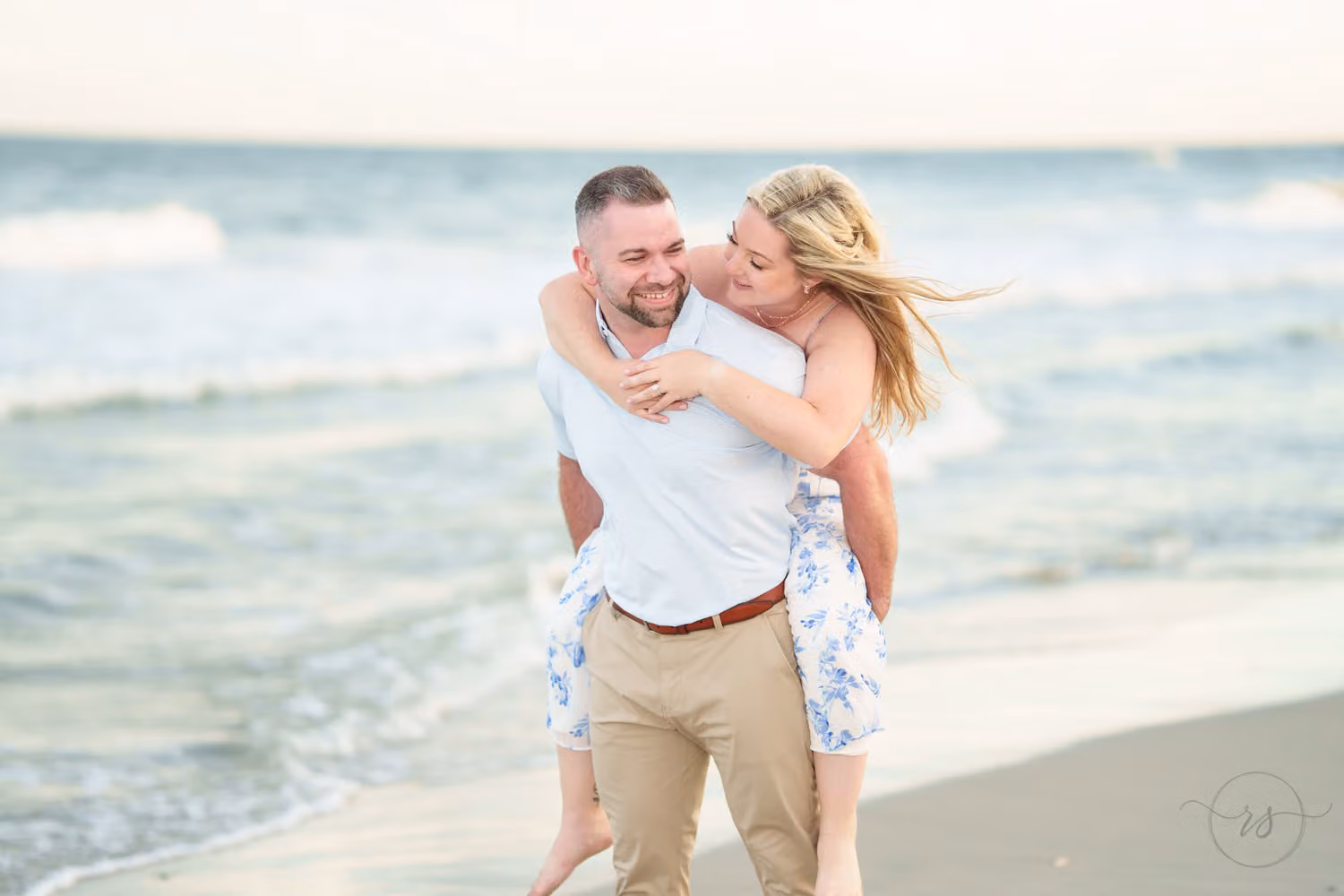 Woman in a floral dress riding piggyback and laughing by the waves at Huntington Beach State Park