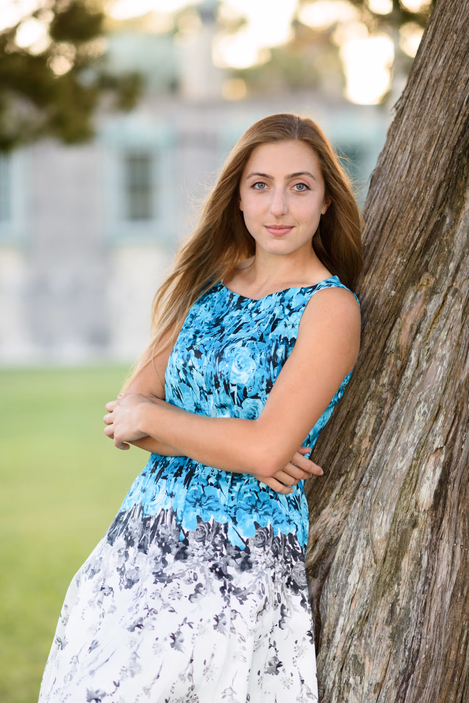 Senior in a floral dress leaning against a tree trunk with the castle soft behind her at Atalaya Castle