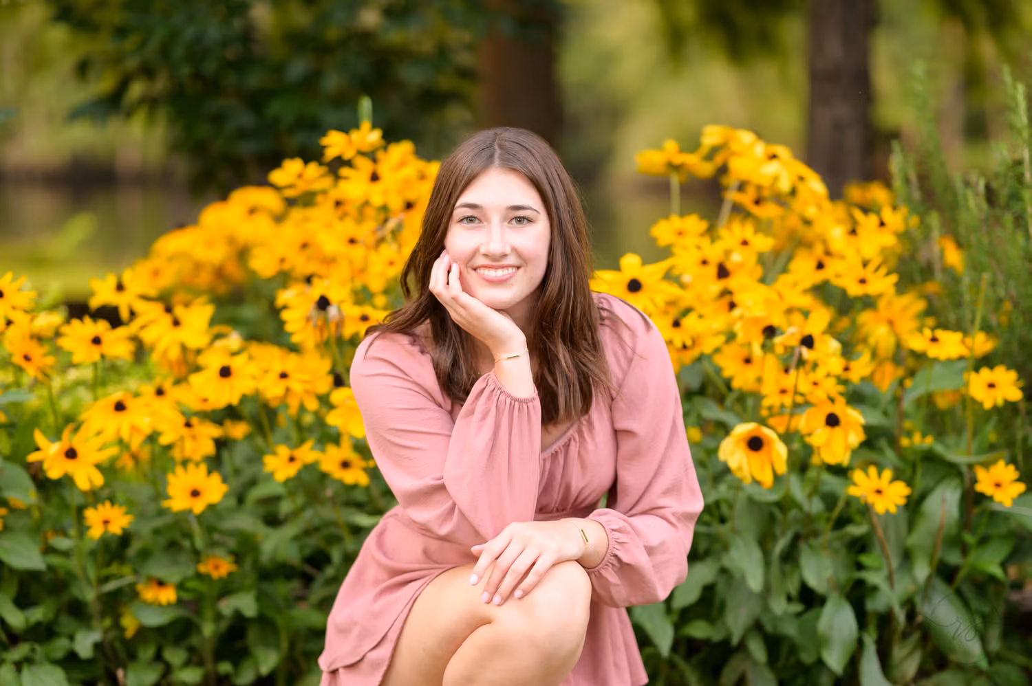 Senior girl in a pink dress crouching among bright yellow black-eyed Susans at the Conway River Walk