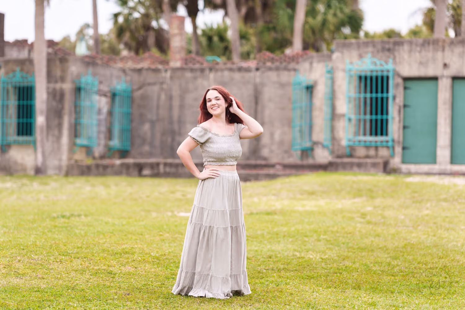Senior in a long skirt with a hand in her hair on the lawn behind the castle at Atalaya Castle