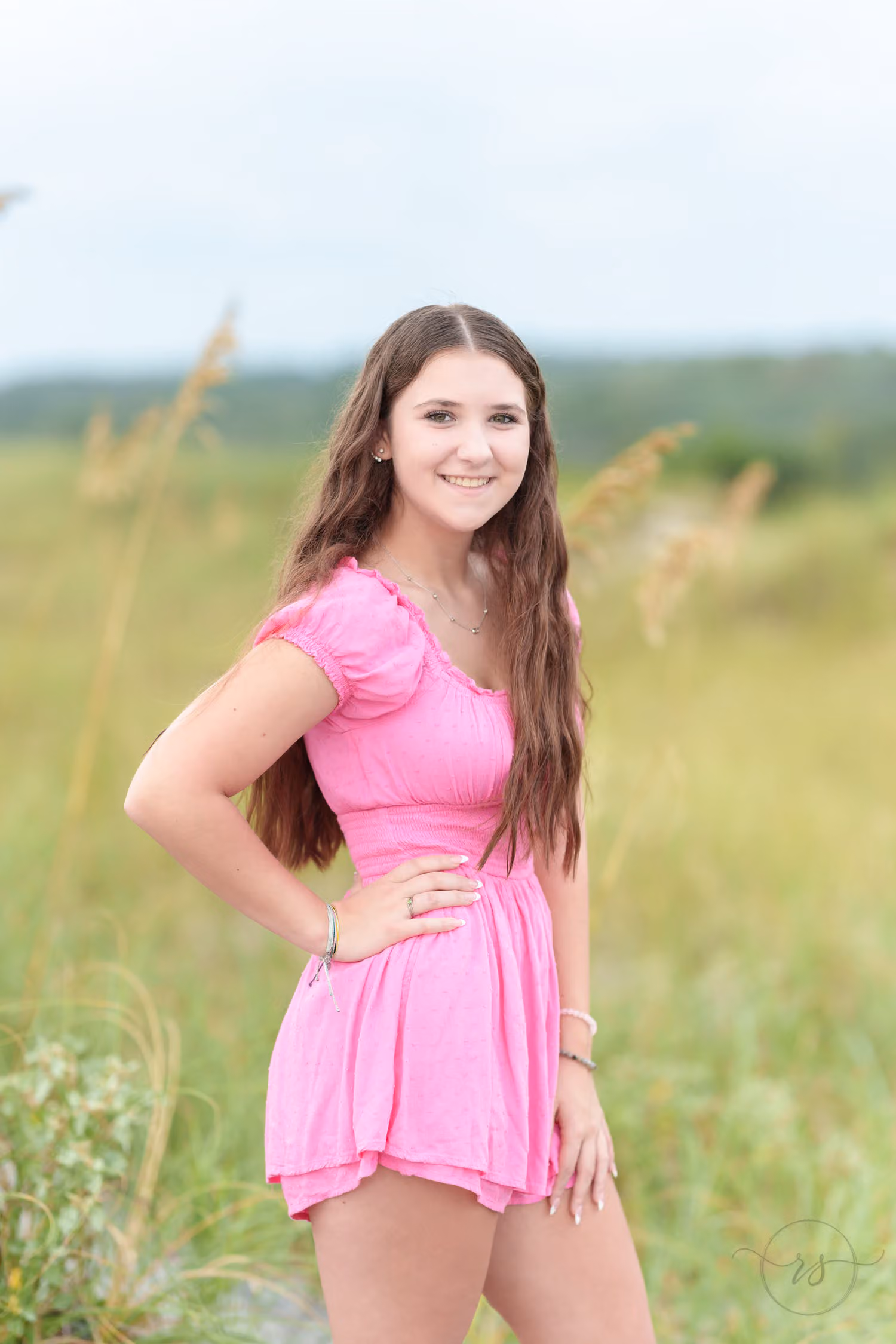 Senior in a pink romper with a hand on her hip in the tall grass and sea oats at Huntington Beach State Park