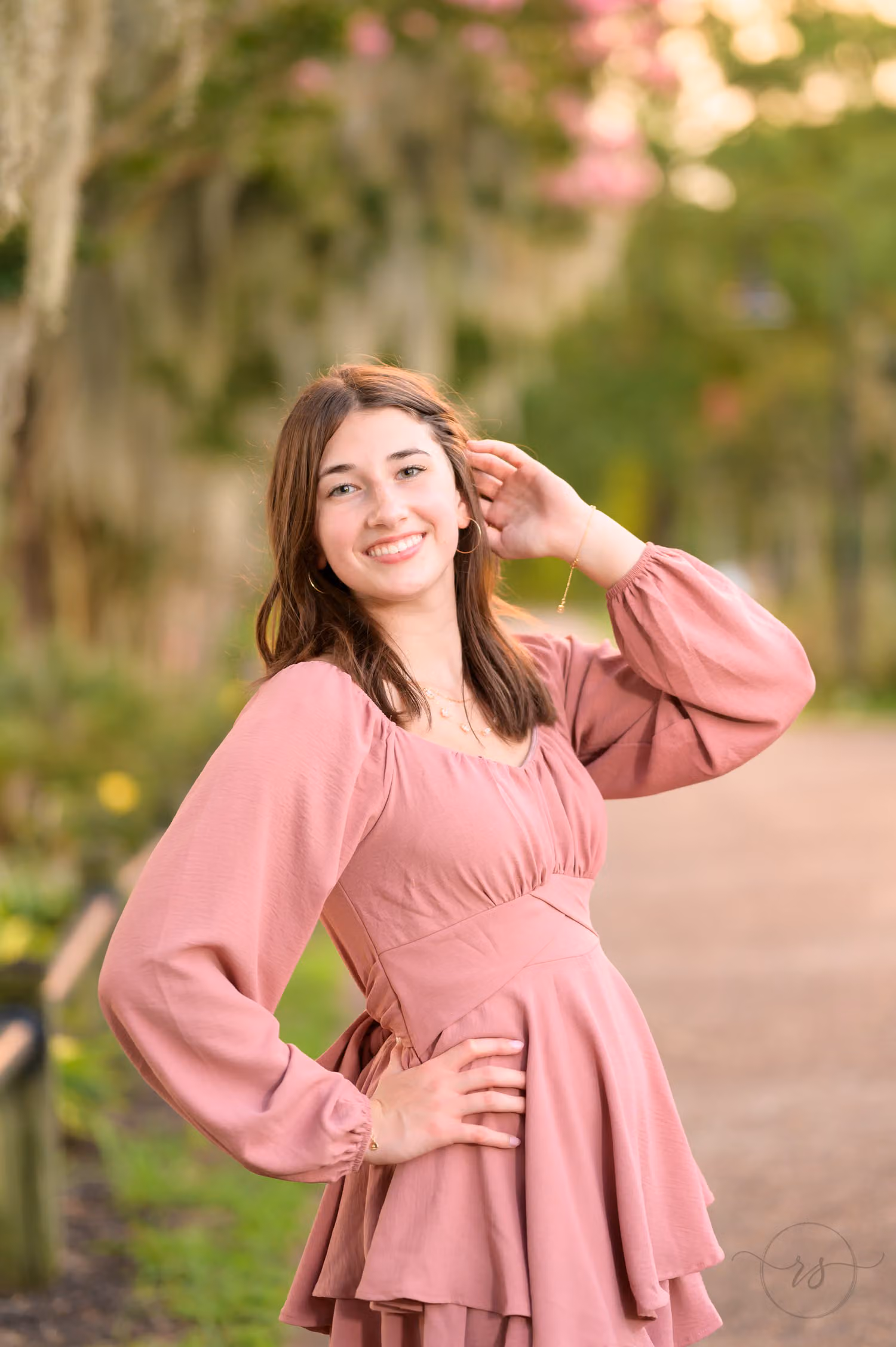 Senior girl in a pink dress with her hand in her hair in warm evening light along the Conway River Walk