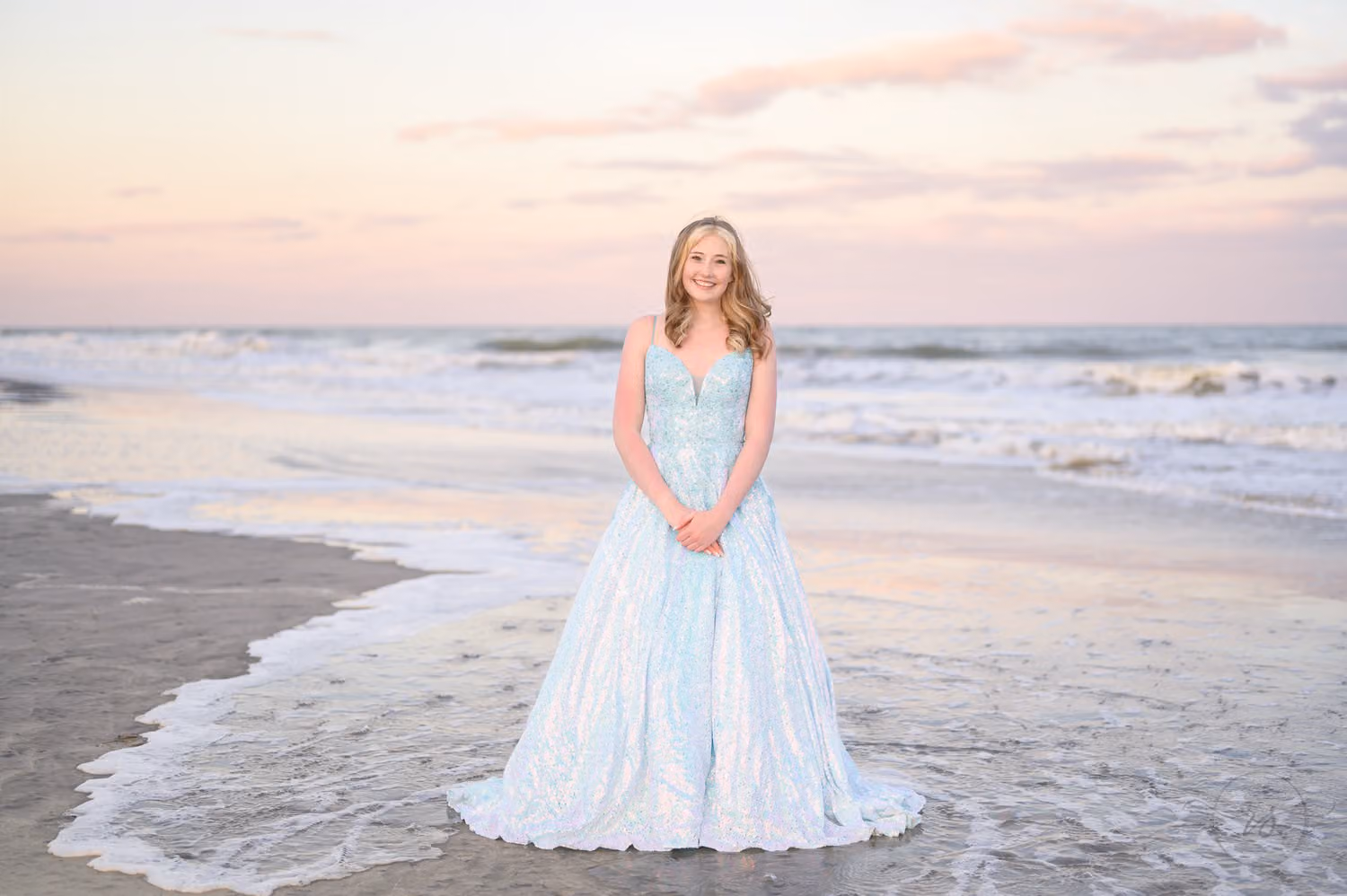 Teen in a blue prom gown standing where the waves wash up on the beach at sunset at Huntington Beach State Park