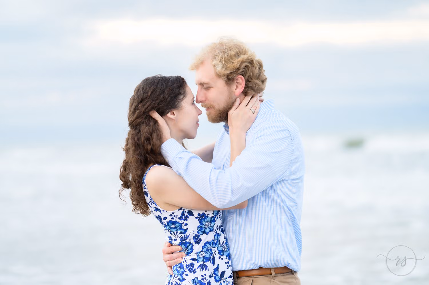 Couple holding each other's faces and touching noses by the ocean on a cloudy day at Huntington Beach State Park
