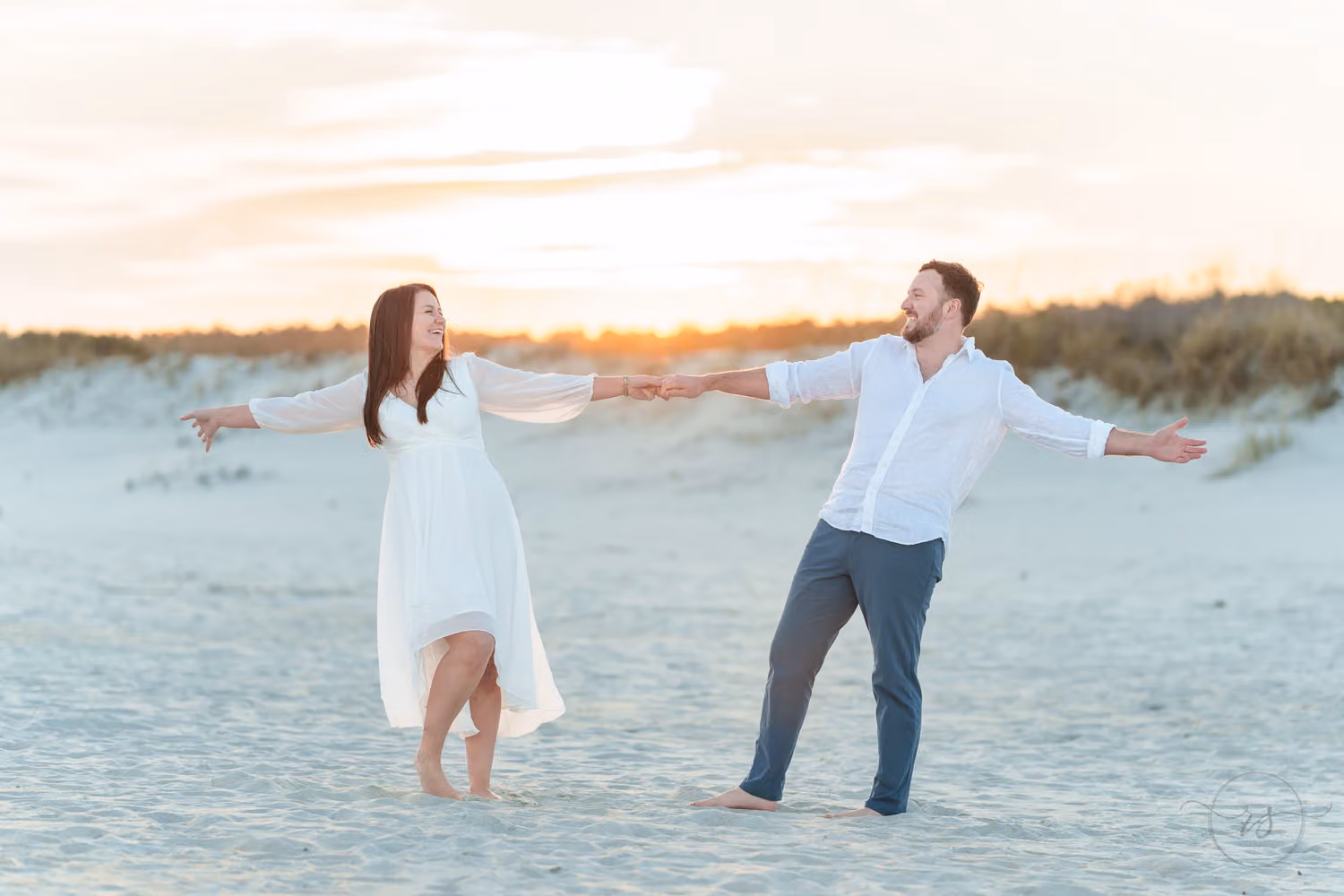 Couple reaching toward each other with outstretched arms on the beach in sunset light at Huntington Beach State Park