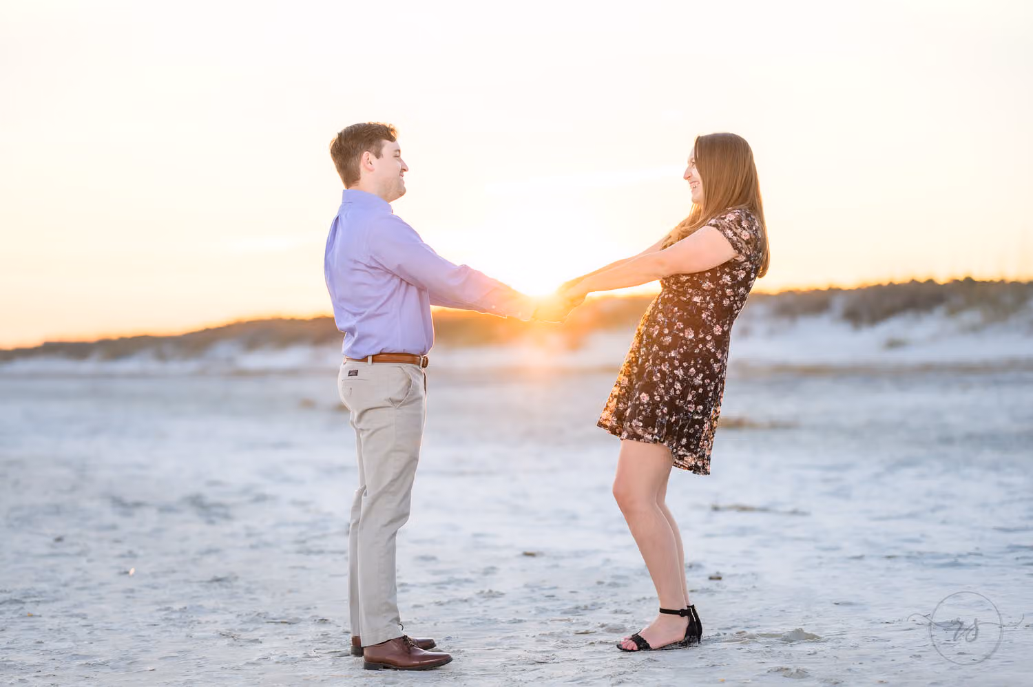 Couple reaching for each other's hands with the sun setting over the dunes between them at Huntington Beach State Park