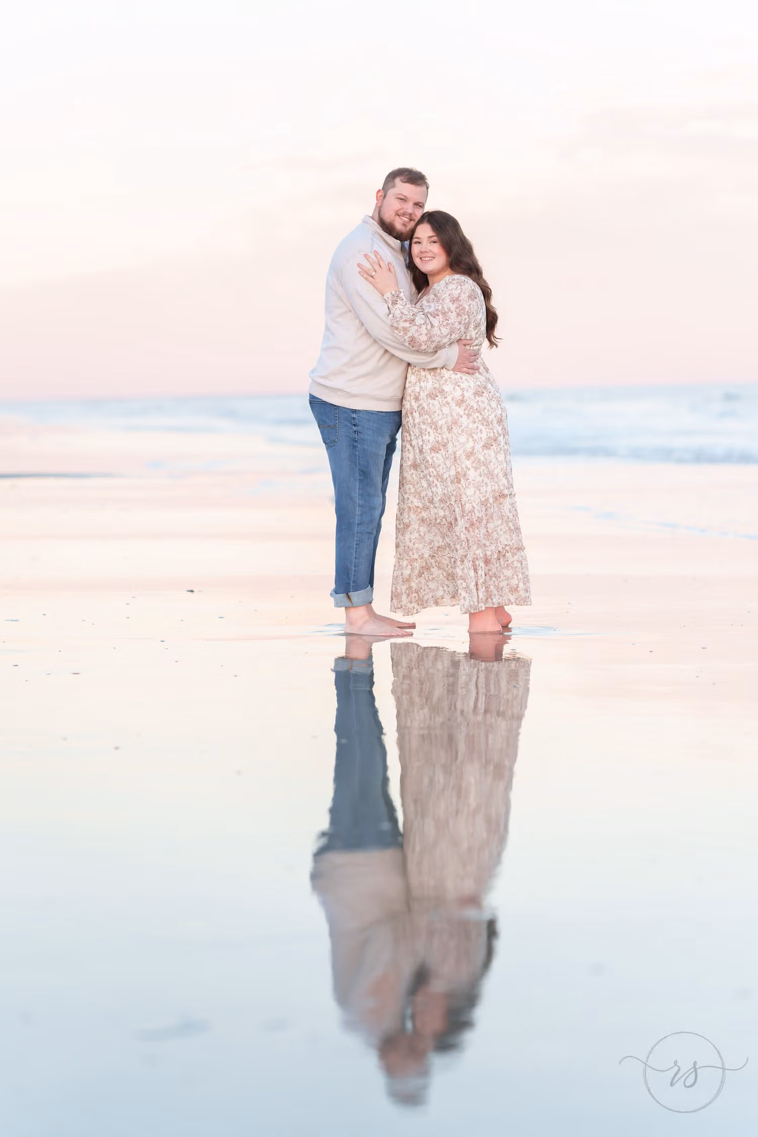 Couple hugging on wet sand at dusk with their full reflection mirrored below them at Huntington Beach State Park