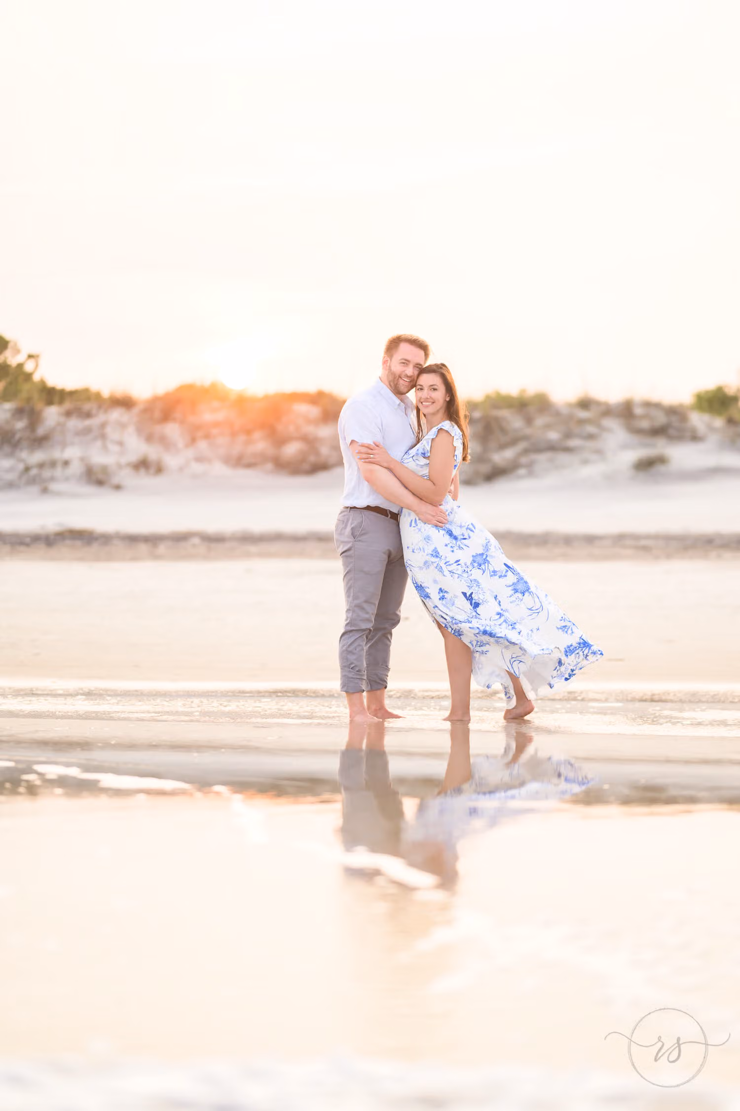 Couple embracing on the wet sand with their reflection and a sunset glow over the dunes at Huntington Beach State Park