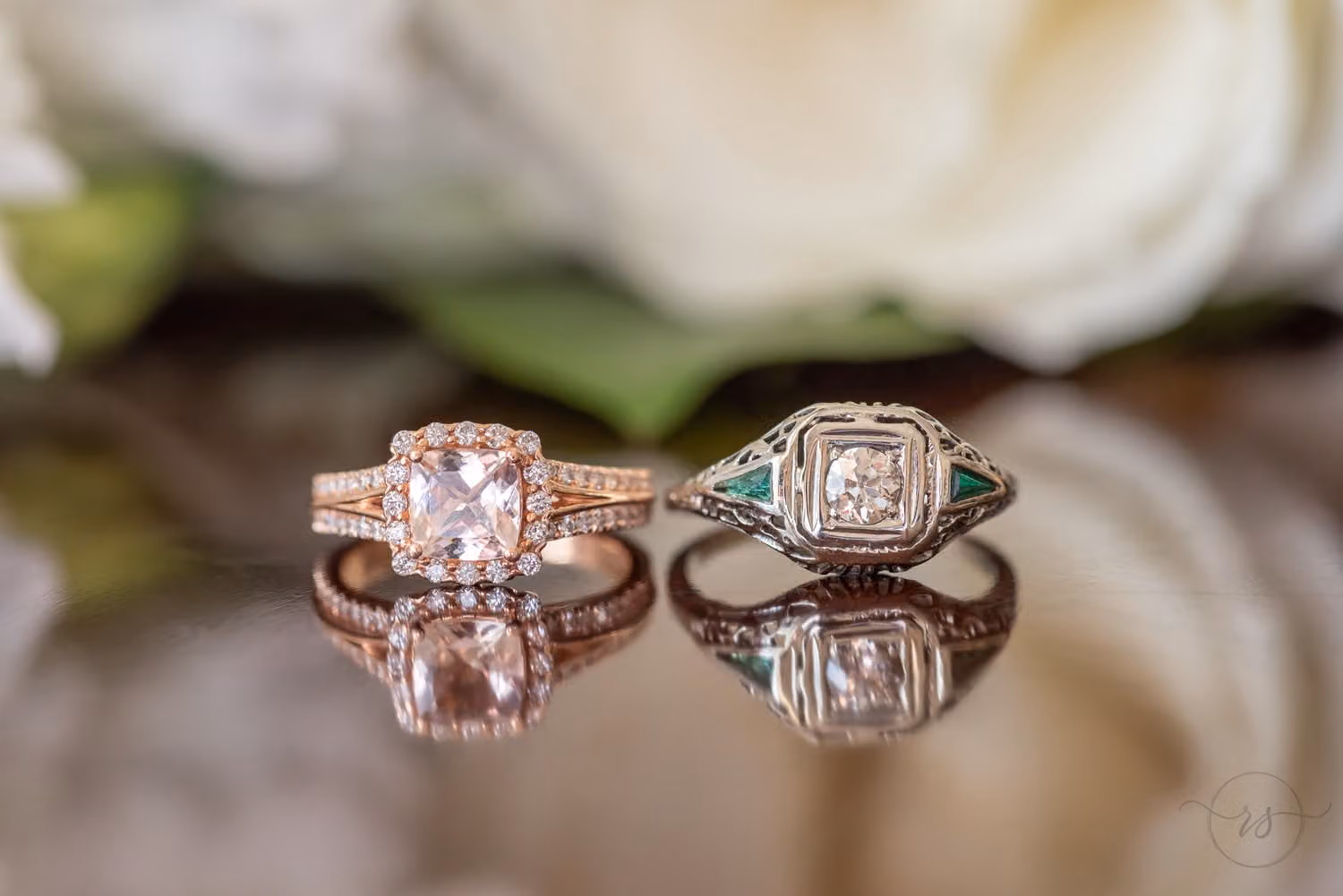 Two diamond rings, one rose gold, reflected on a glossy surface under white flowers at Kimbel's at Wachesaw Plantation
