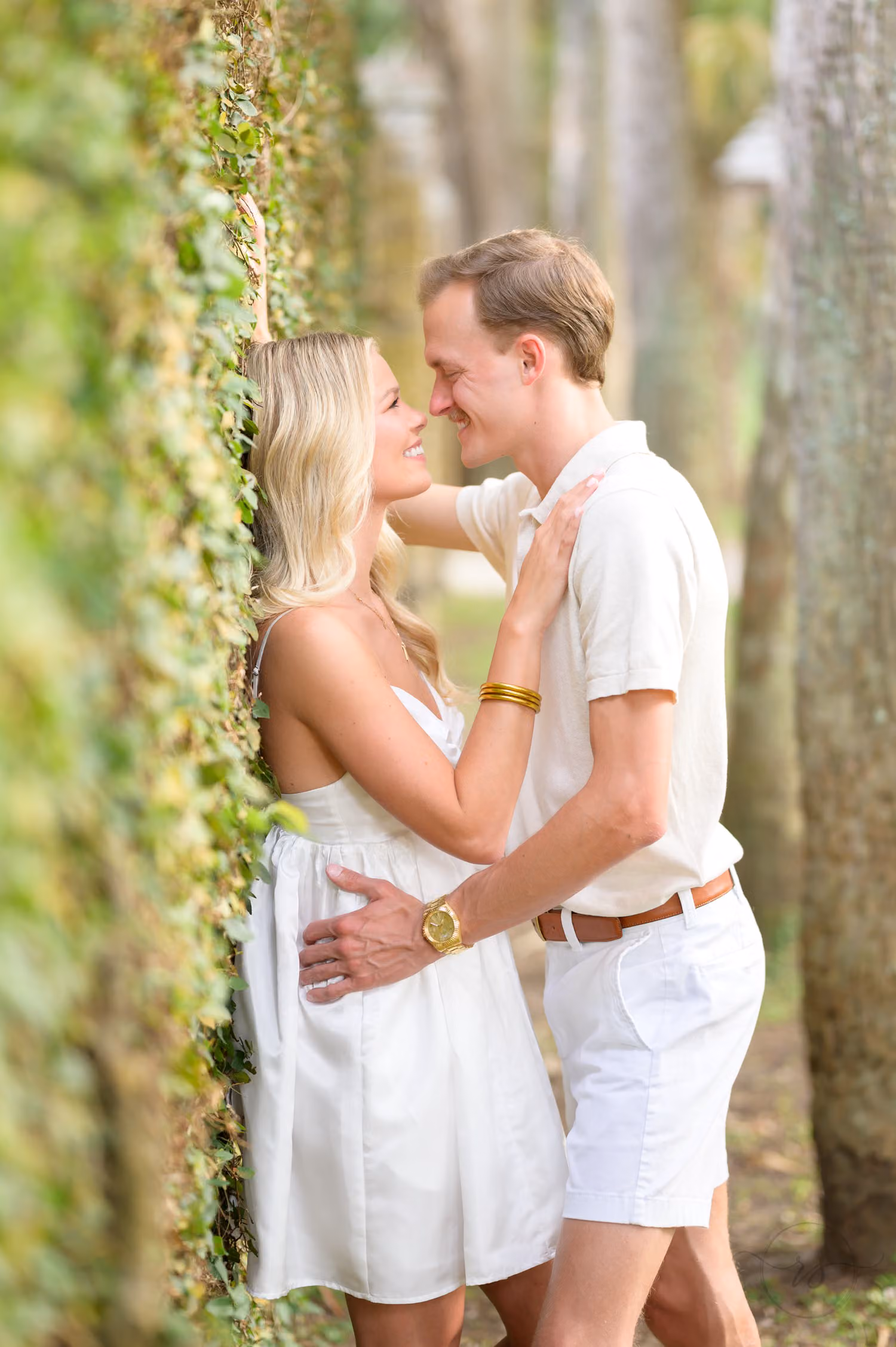 Couple in white leaning in close beside an ivy-covered wall in the woods at Huntington Beach State Park