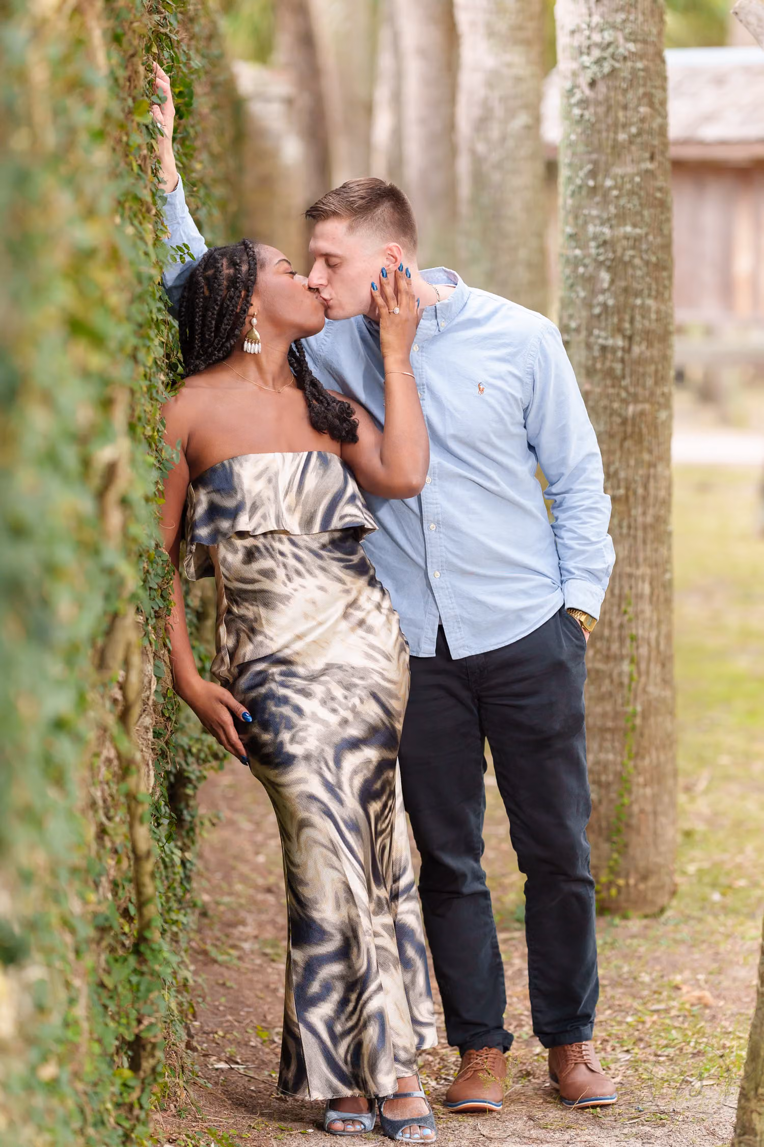 Couple kissing against an ivy-covered wall beside tall trees at Huntington Beach State Park