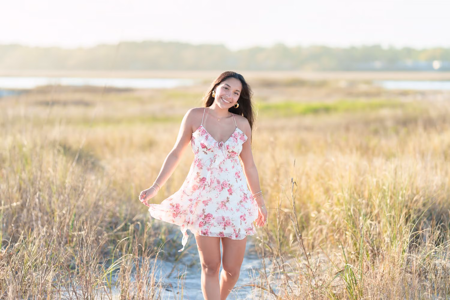 Senior girl in a pink floral dress walking through the golden marsh grass in North Myrtle Beach