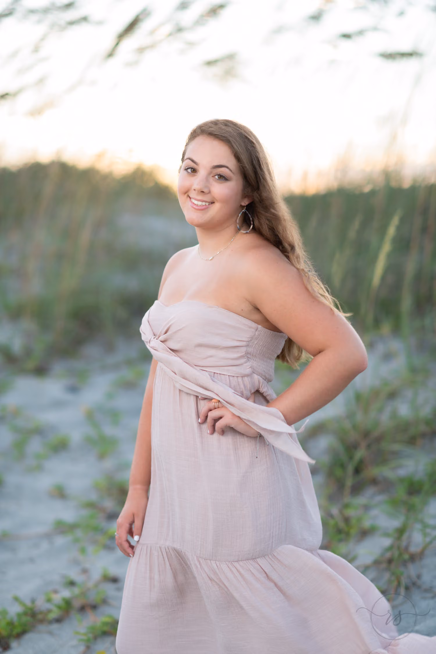 Senior in a blush strapless dress with a hand on her hip by the sea oats at sunset at Huntington Beach State Park
