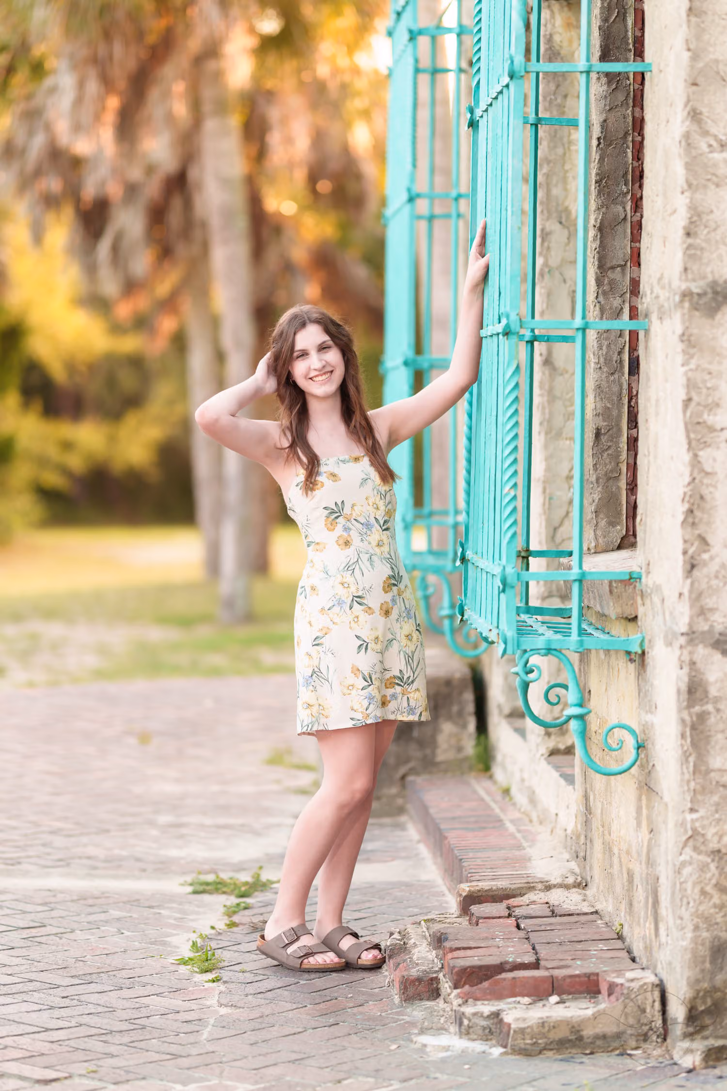 Senior girl in a floral sundress leaning on the teal window grille of Atalaya Castle at Huntington Beach State Park