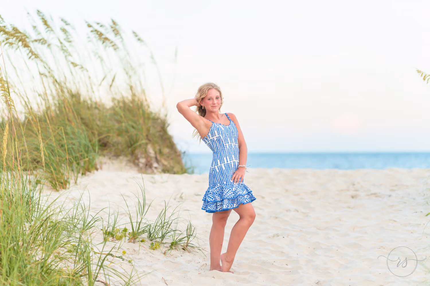Senior girl in a blue sundress posing on the sand beside the sea oats at Huntington Beach State Park