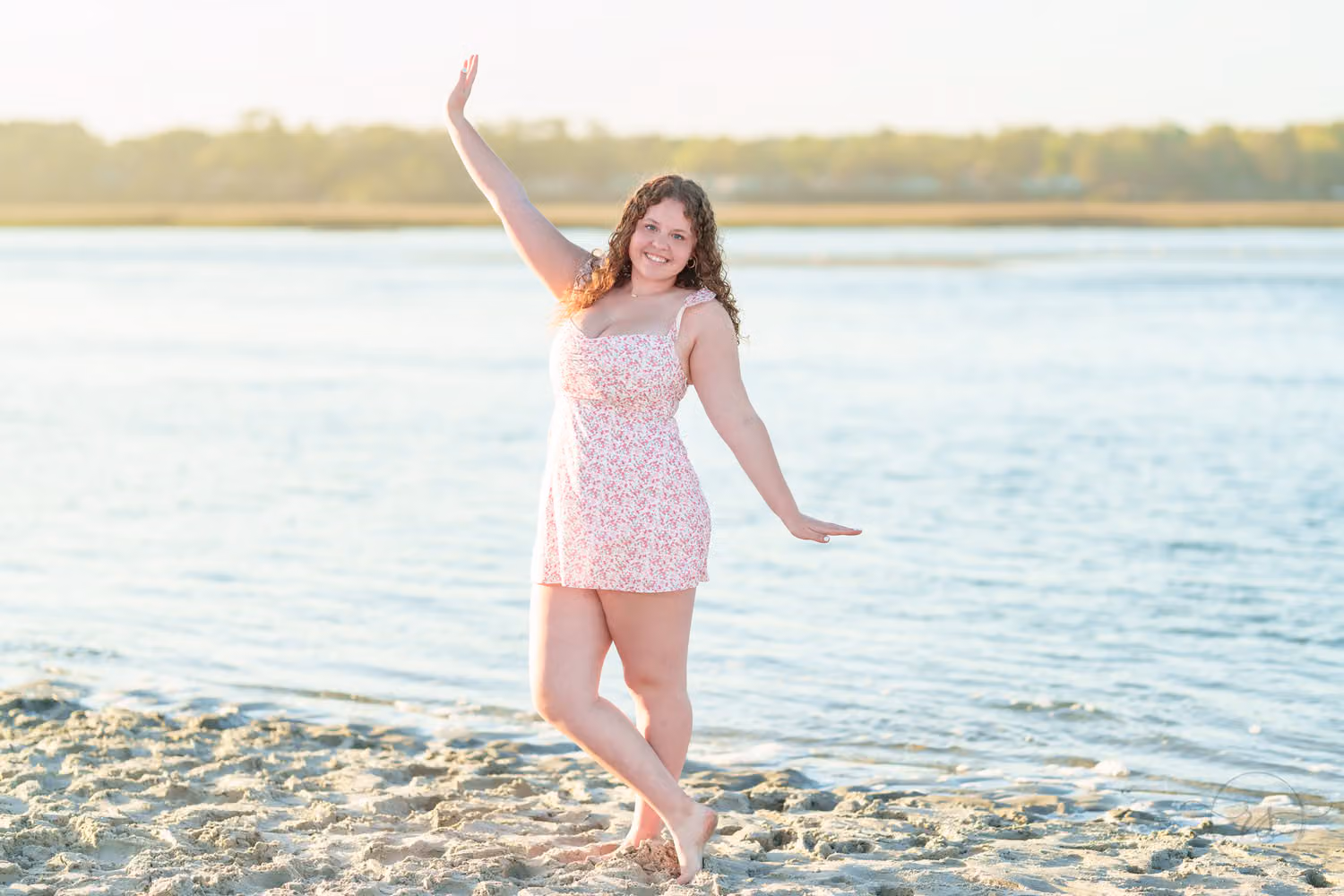 Senior girl in a pink floral dress posing with one arm raised at the edge of the inlet in North Myrtle Beach