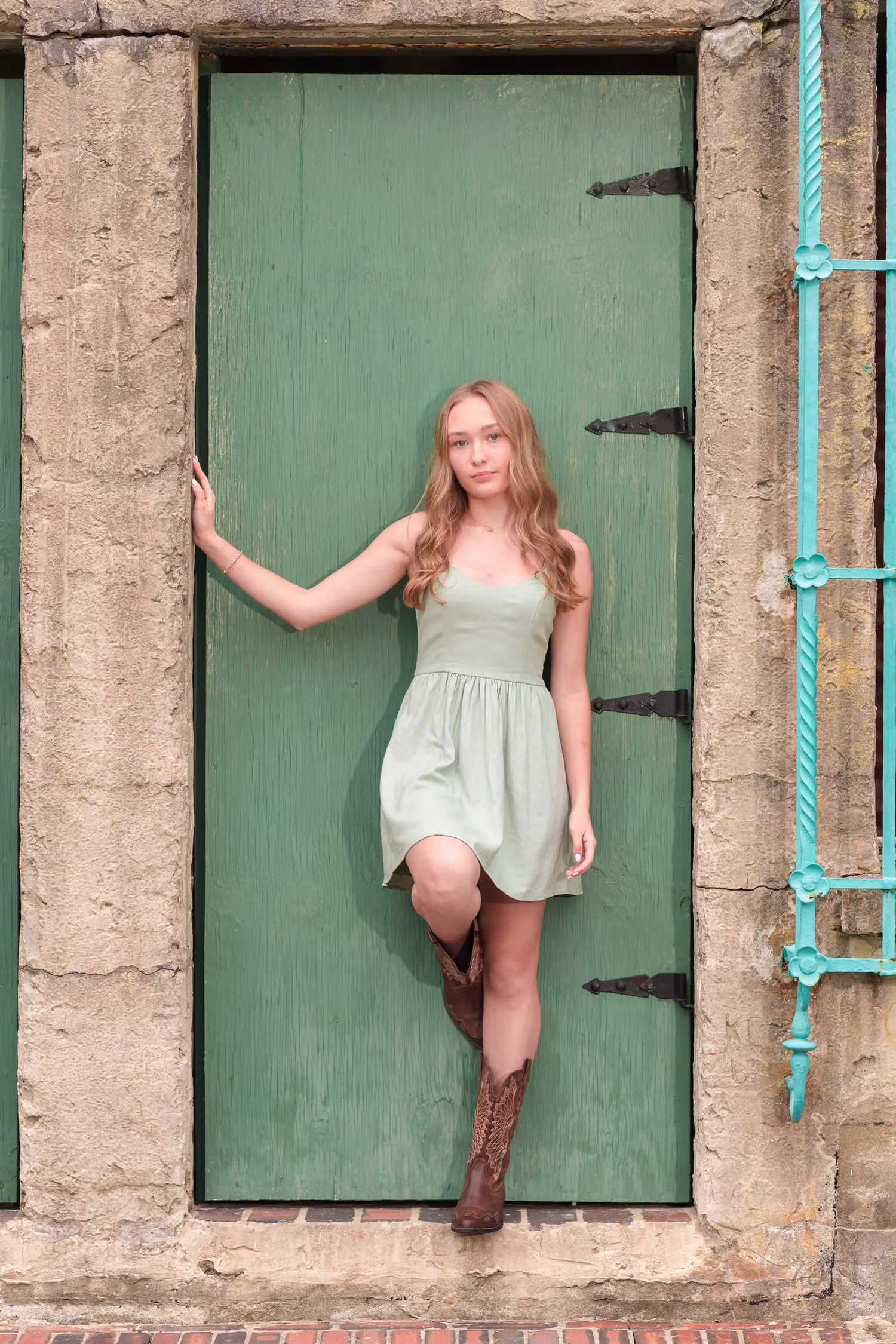Senior girl in a mint dress and cowboy boots standing in the green doorway of Atalaya Castle at Huntington Beach State Park