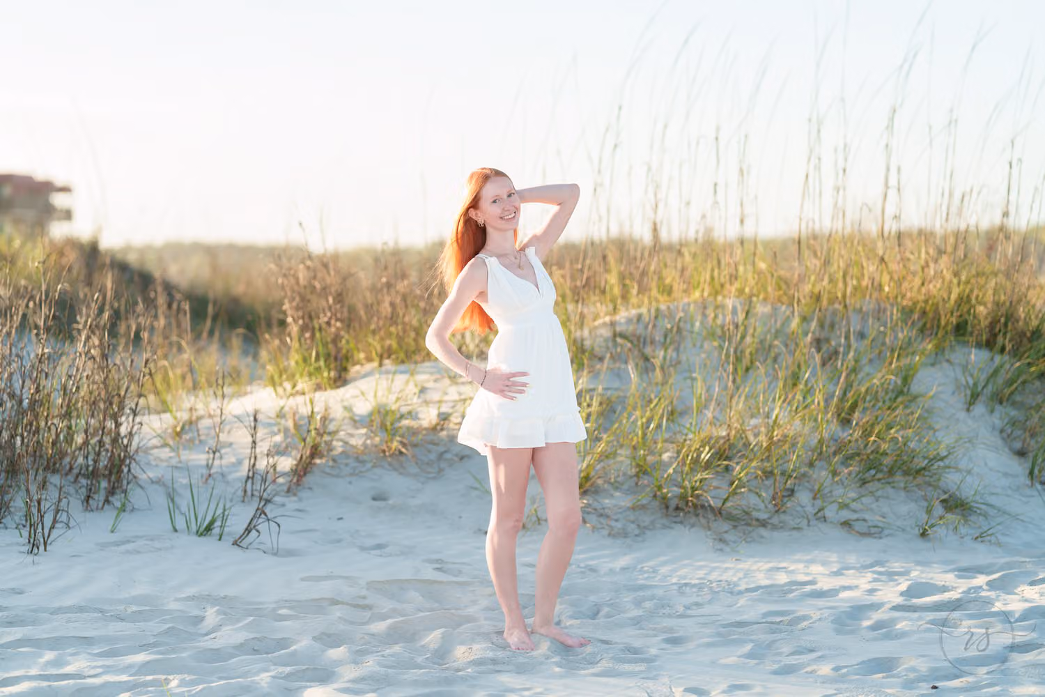 Red-haired senior girl in a white dress standing among the sea oats on the dunes in North Myrtle Beach