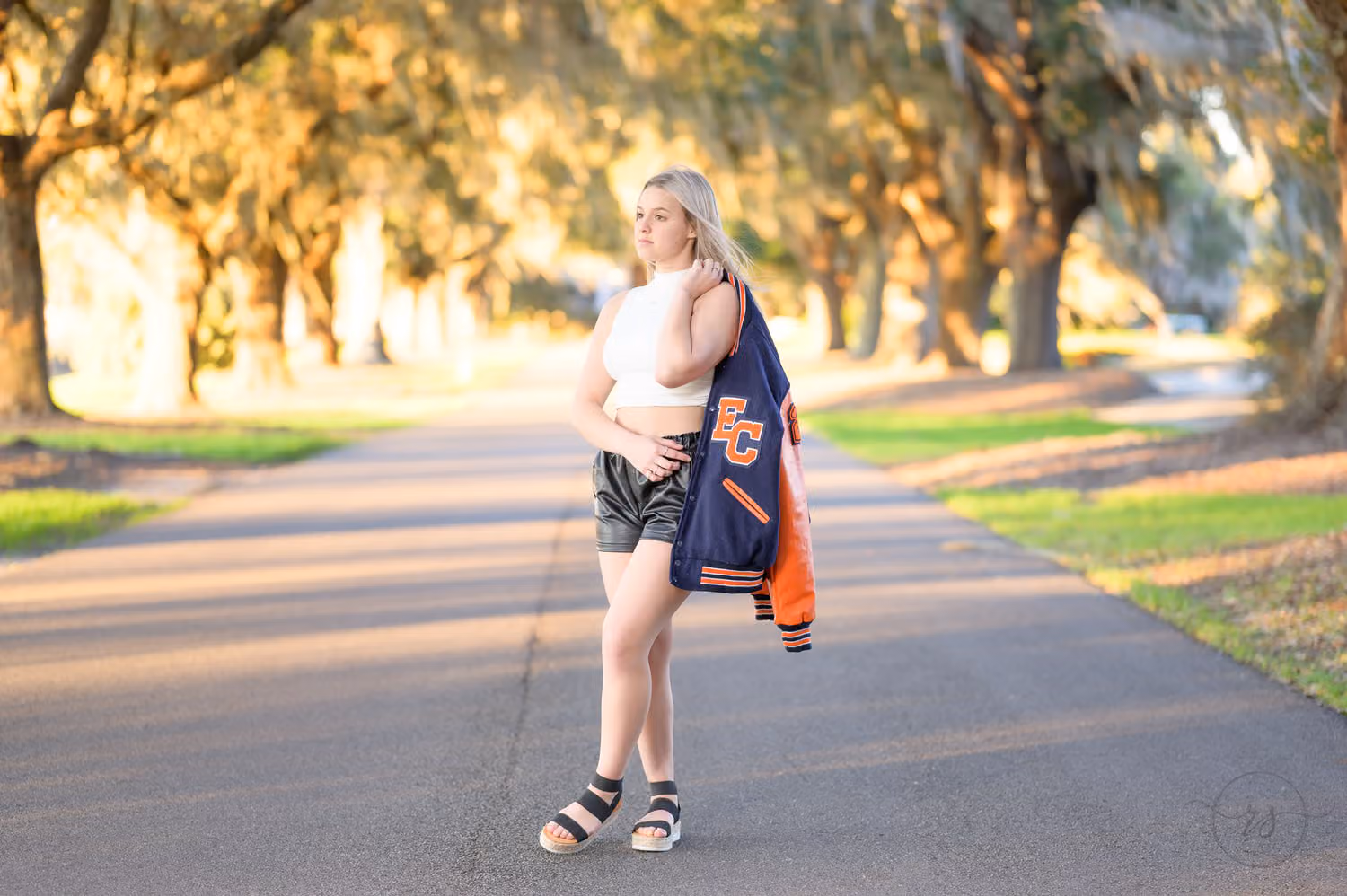 Senior girl holding her letterman jacket over her shoulder on the oak-lined road at Caledonia Golf & Fish Club