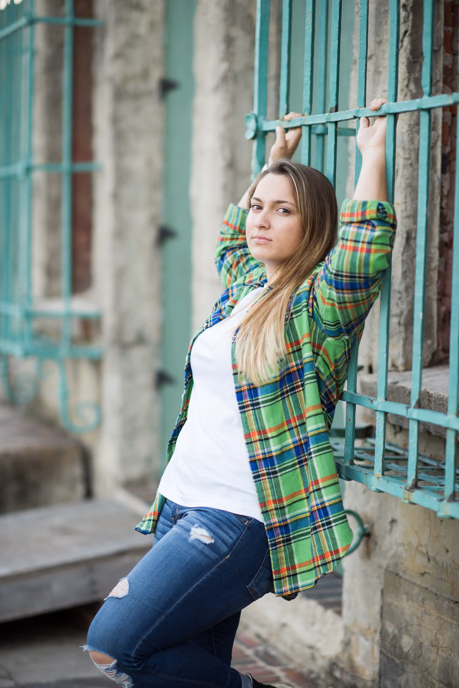 Senior in a green plaid flannel holding the green iron window grate above her head at Atalaya Castle