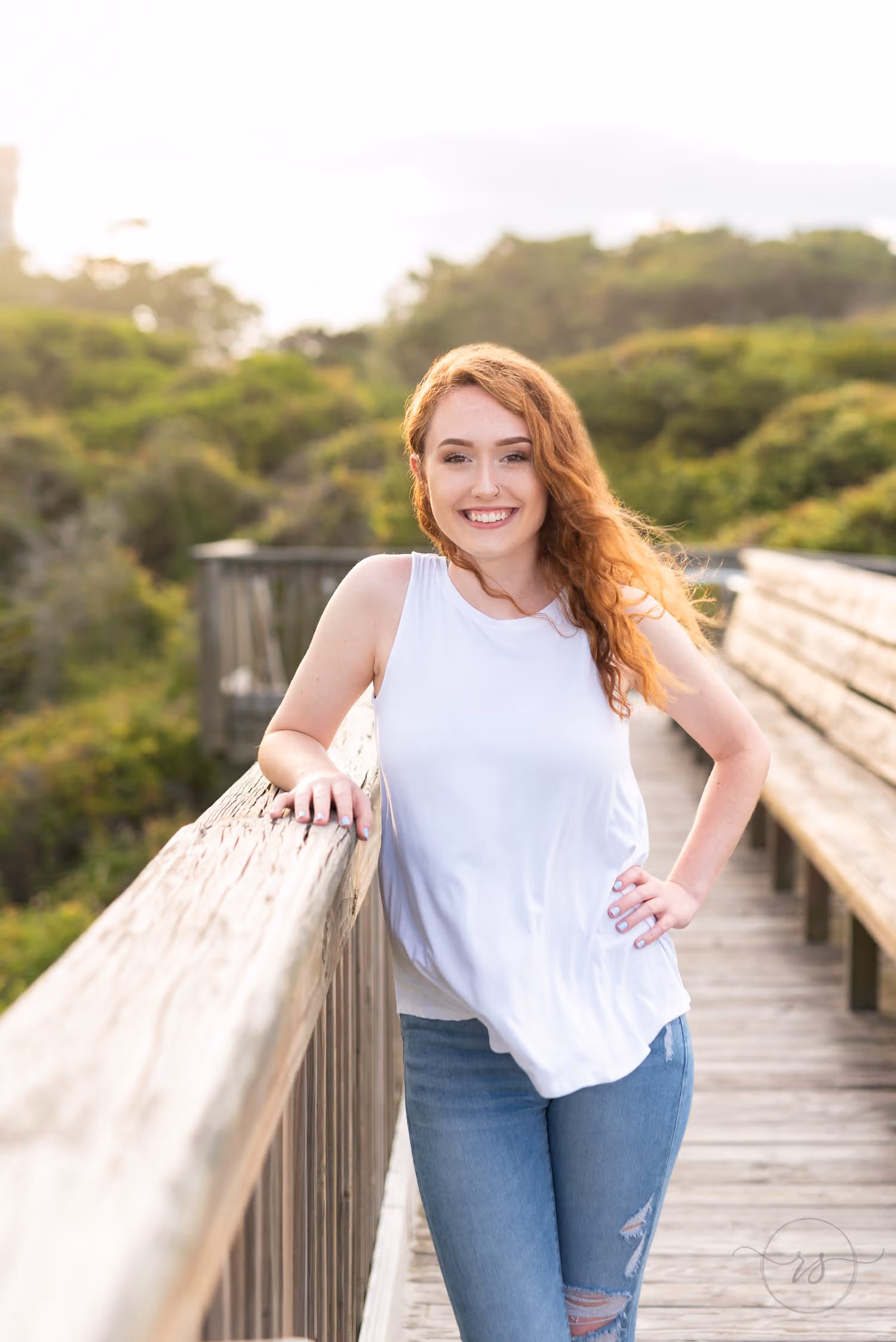 Red-haired senior in a white tank top and jeans leaning on a boardwalk rail at Grande Dunes in Myrtle Beach