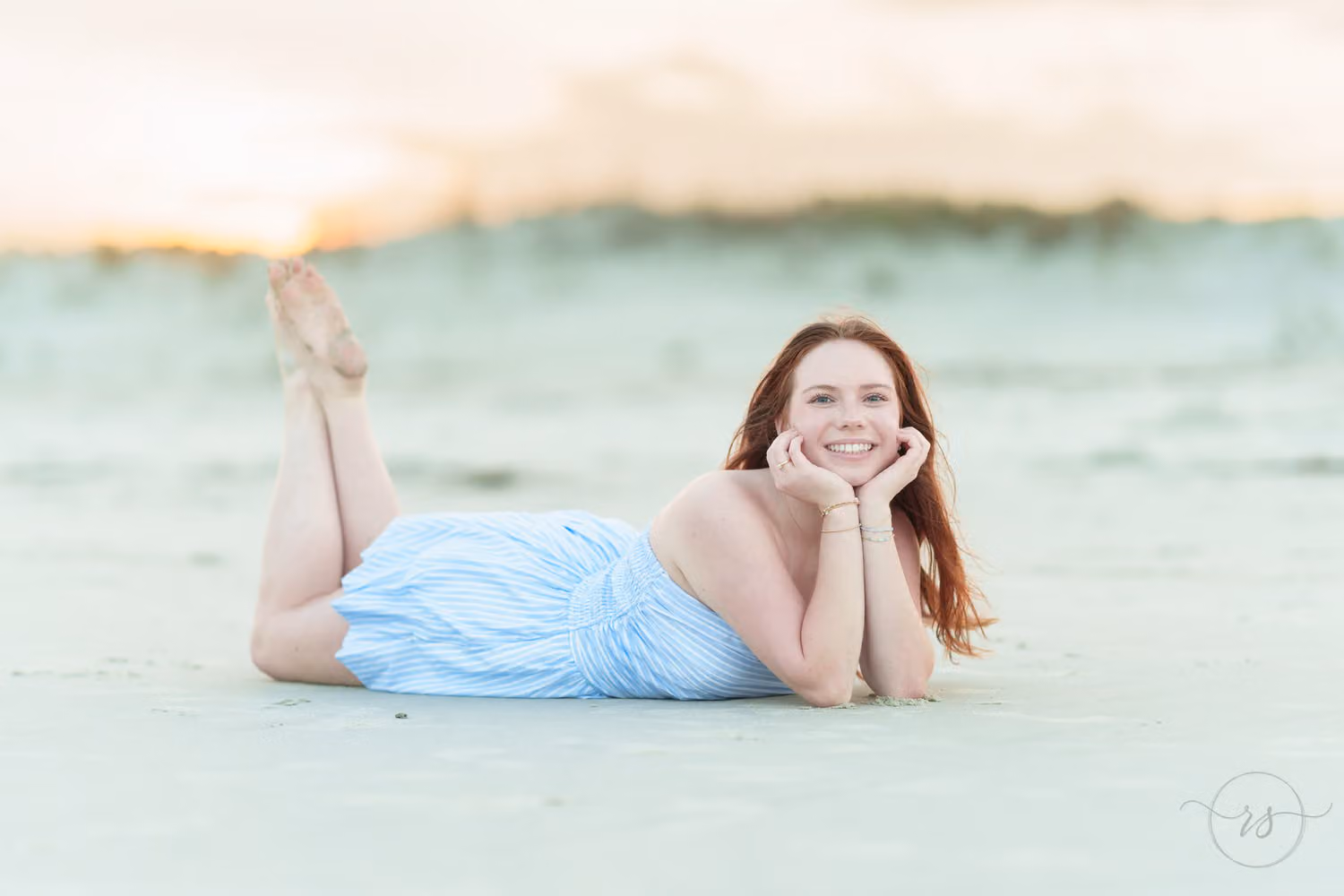 Senior girl lying on her stomach in the sand with her feet up and chin in her hands at Huntington Beach State Park