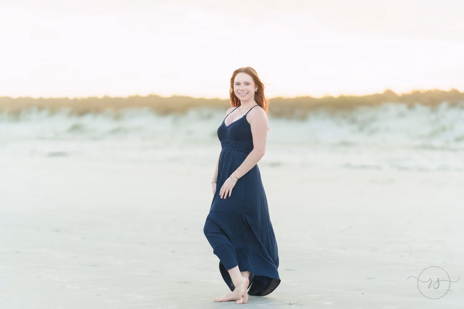 High school senior in a long navy dress standing on the beach in front of the dunes at Huntington Beach State Park