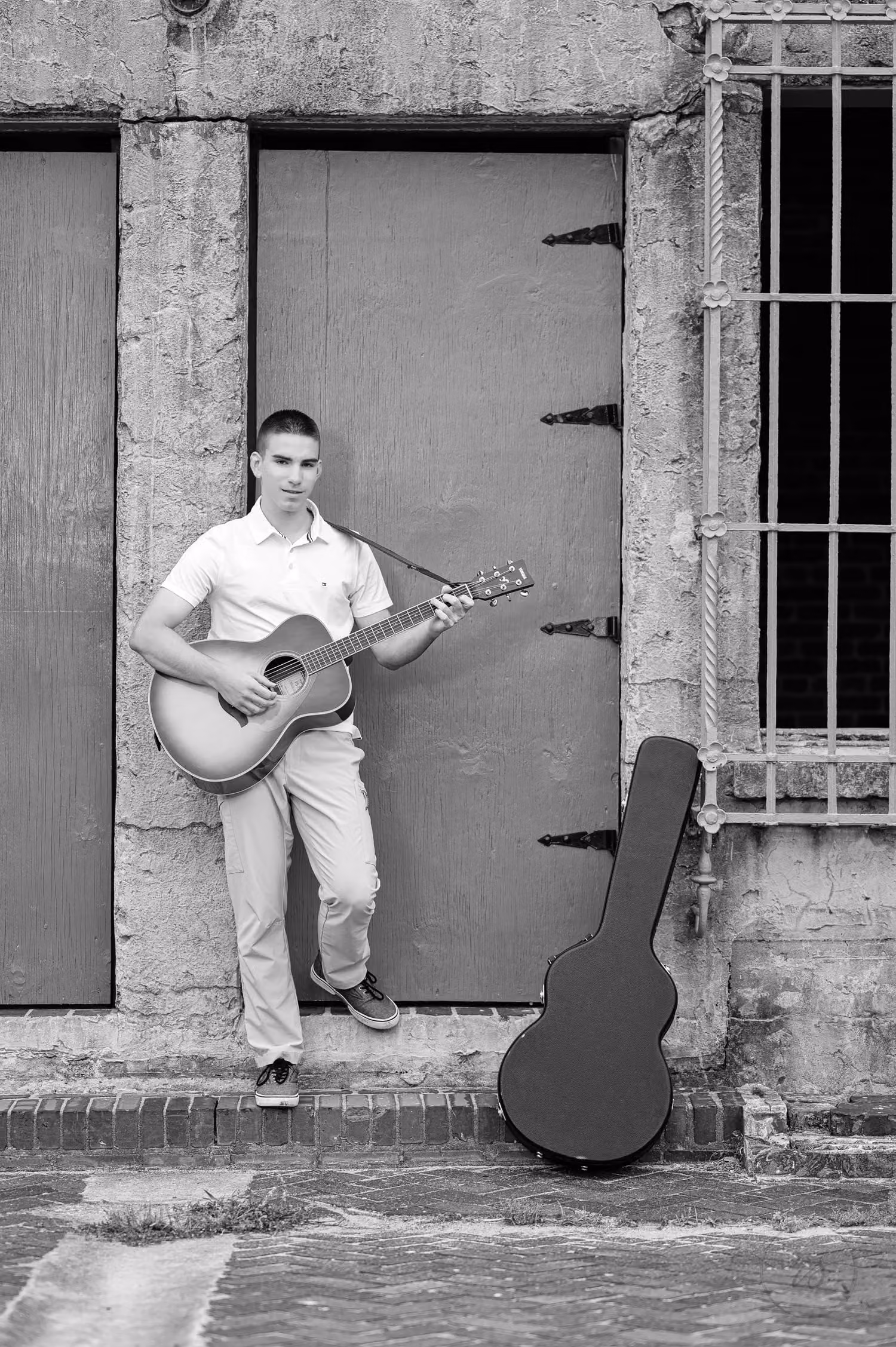 Black and white photo of a senior playing guitar by the castle door, his case beside him at Atalaya Castle