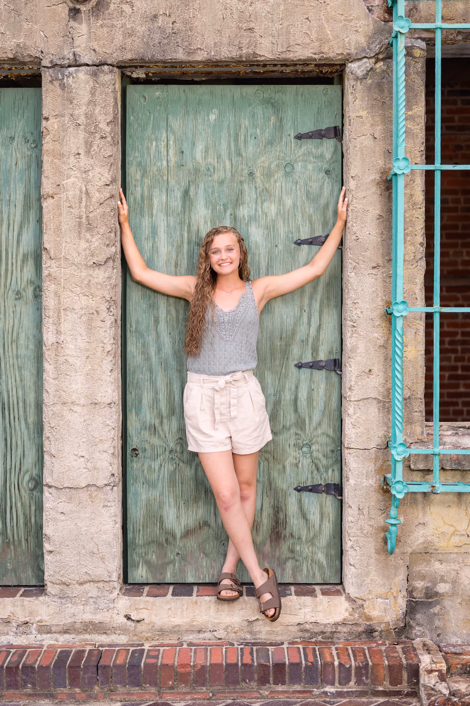 Senior girl with her arms stretched across the green doorway of Atalaya Castle at Huntington Beach State Park