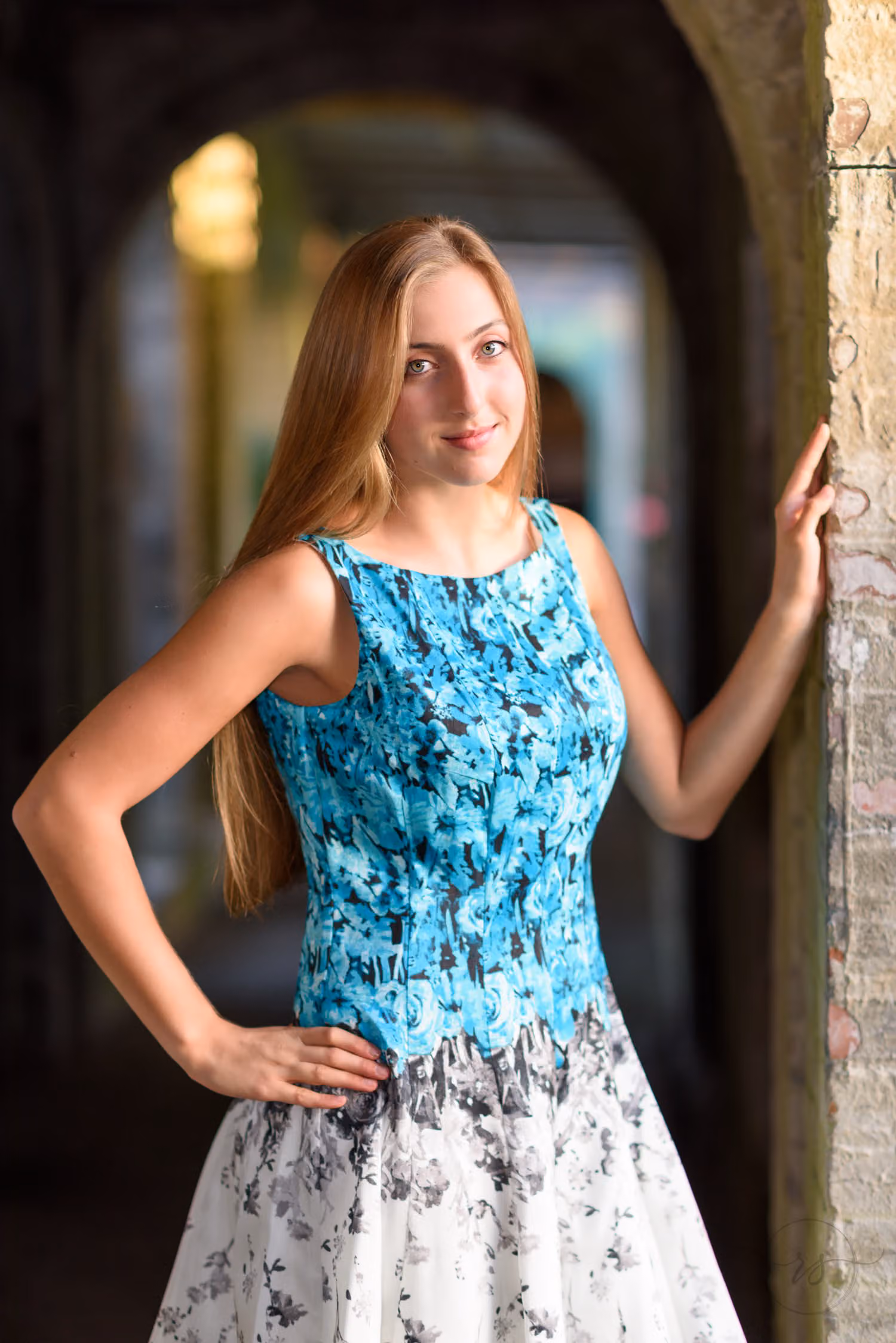 Senior in a floral dress leaning on a brick archway in the long shaded hallway at Atalaya Castle